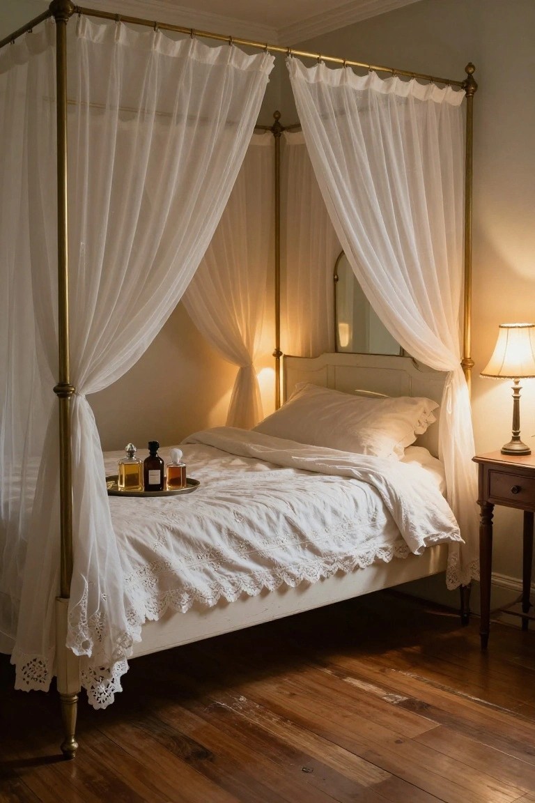 A white four-poster bed with sheer white canopy curtains draped from brass posts, white linens, a silver tray holding perfume bottles on the bed, a bedside lamp, and wooden nightstand in a bedroom with hardwood floors.