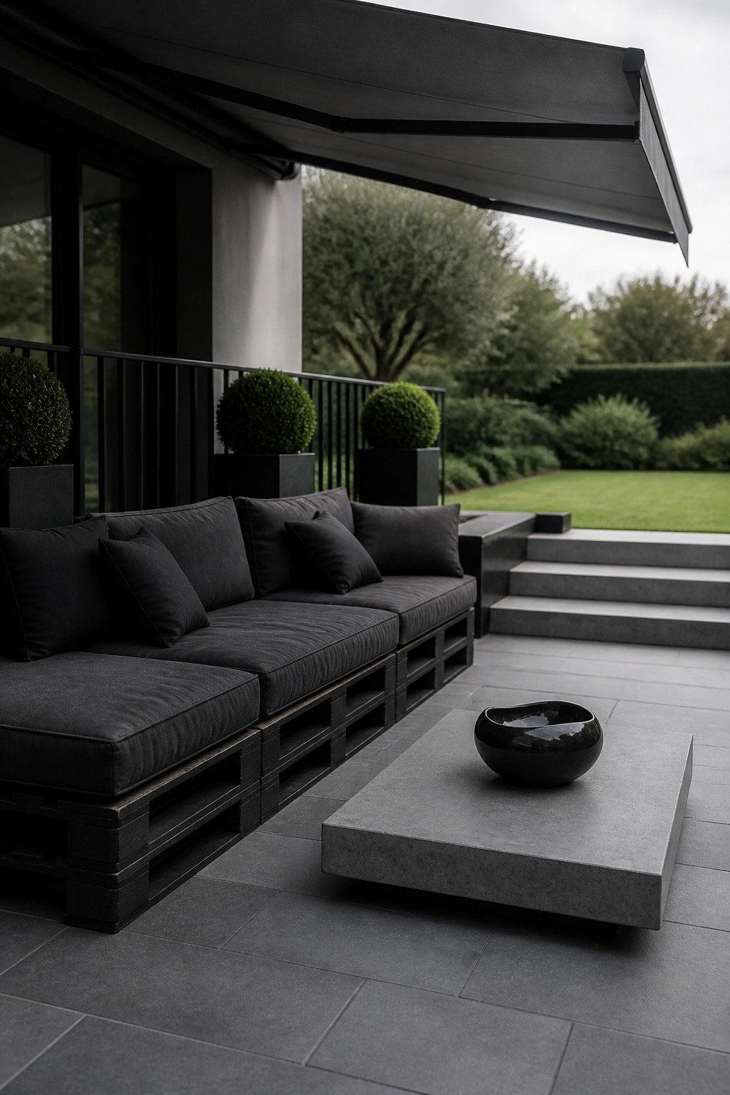 Modern dark patio with black pallet sofa, concrete table, bowl, and garden steps