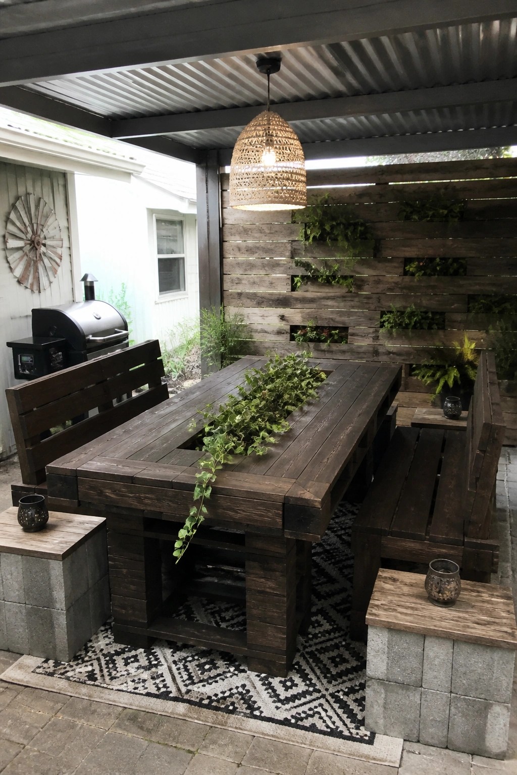 Rustic dark wood patio table with benches under woven hanging light on patterned rug.