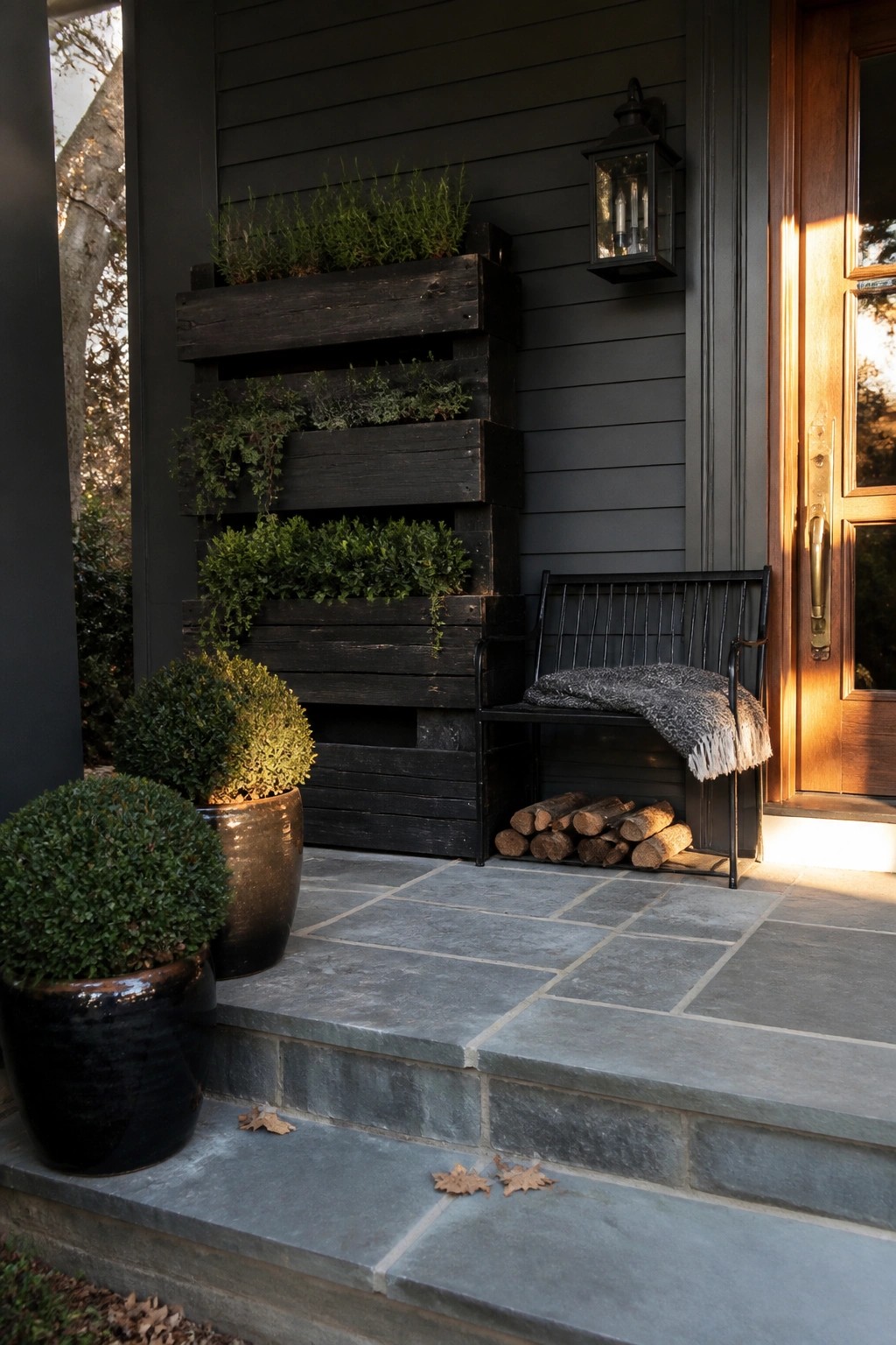 Black bench with blanket beside vertical wood planters on stone porch steps