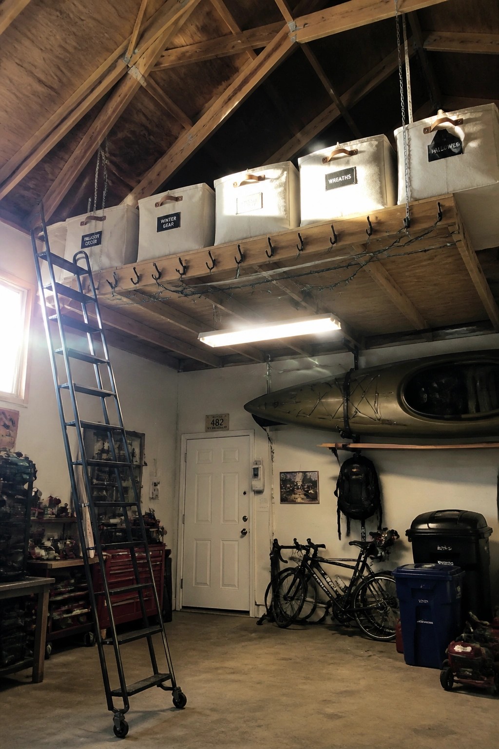 Garage with labeled ceiling bins, rolling ladder, hanging kayak, and bicycles below.