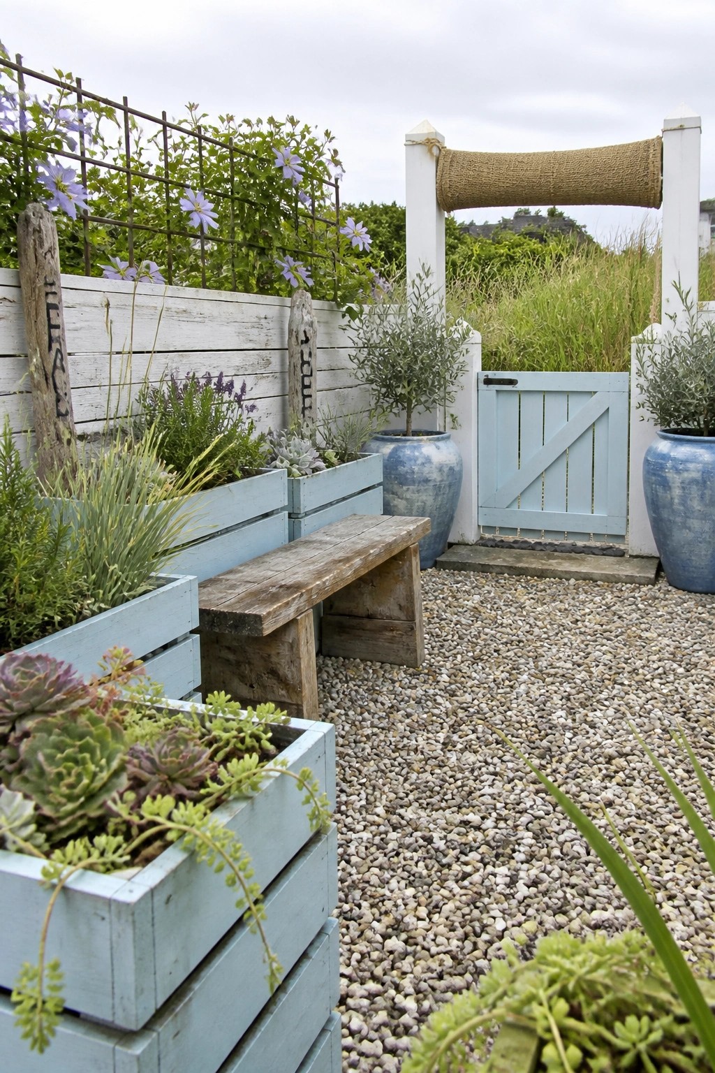 Blue planters, wooden bench, and light blue gate along gravel garden path