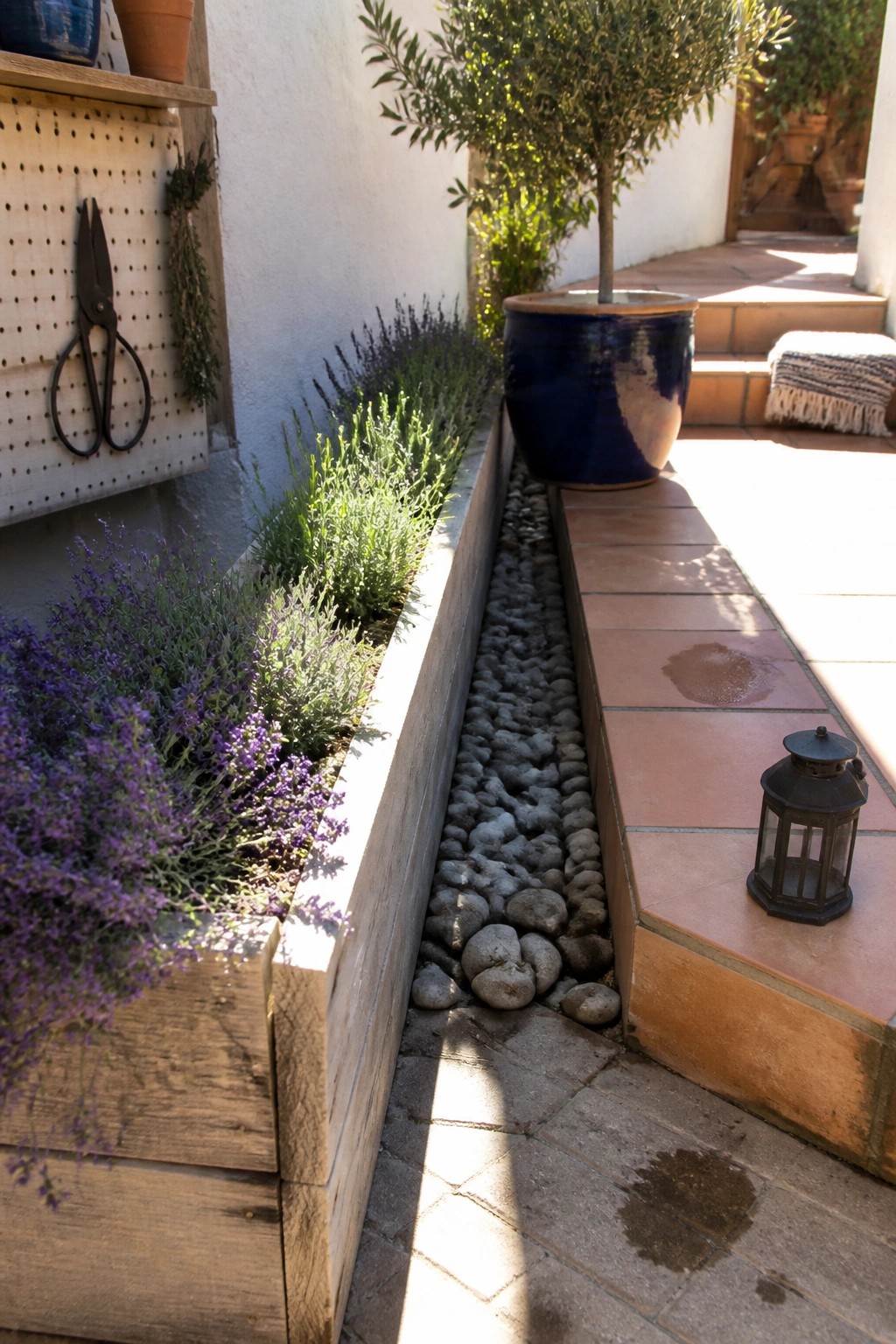A backyard scene with wooden pallet planter boxes filled with lavender and green shrubs, next to a gravel strip and terracotta tile patio.