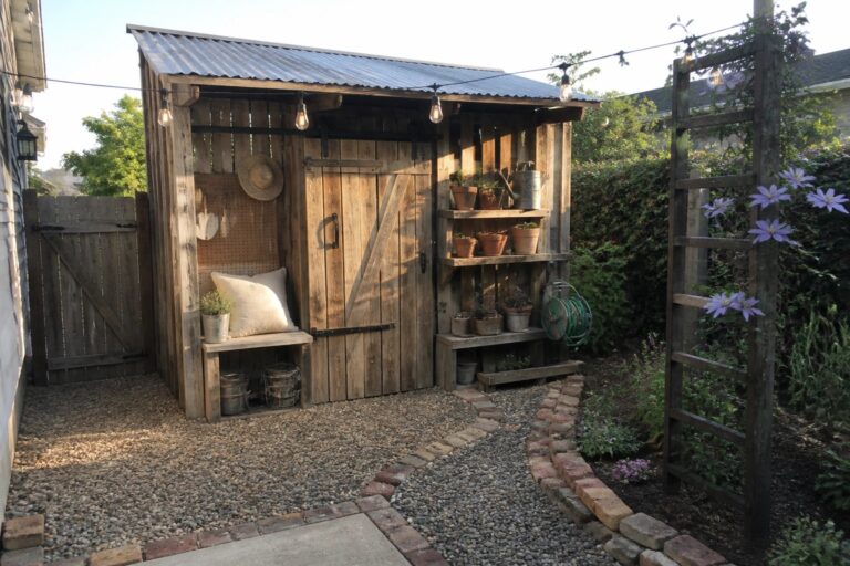 18 Functional Pallet Shed Ideas for Compact Backyard Storage A wooden pallet shed in a backyard with a pegboard holding garden tools, shelves with potted plants, and a coiled hose beside the door.