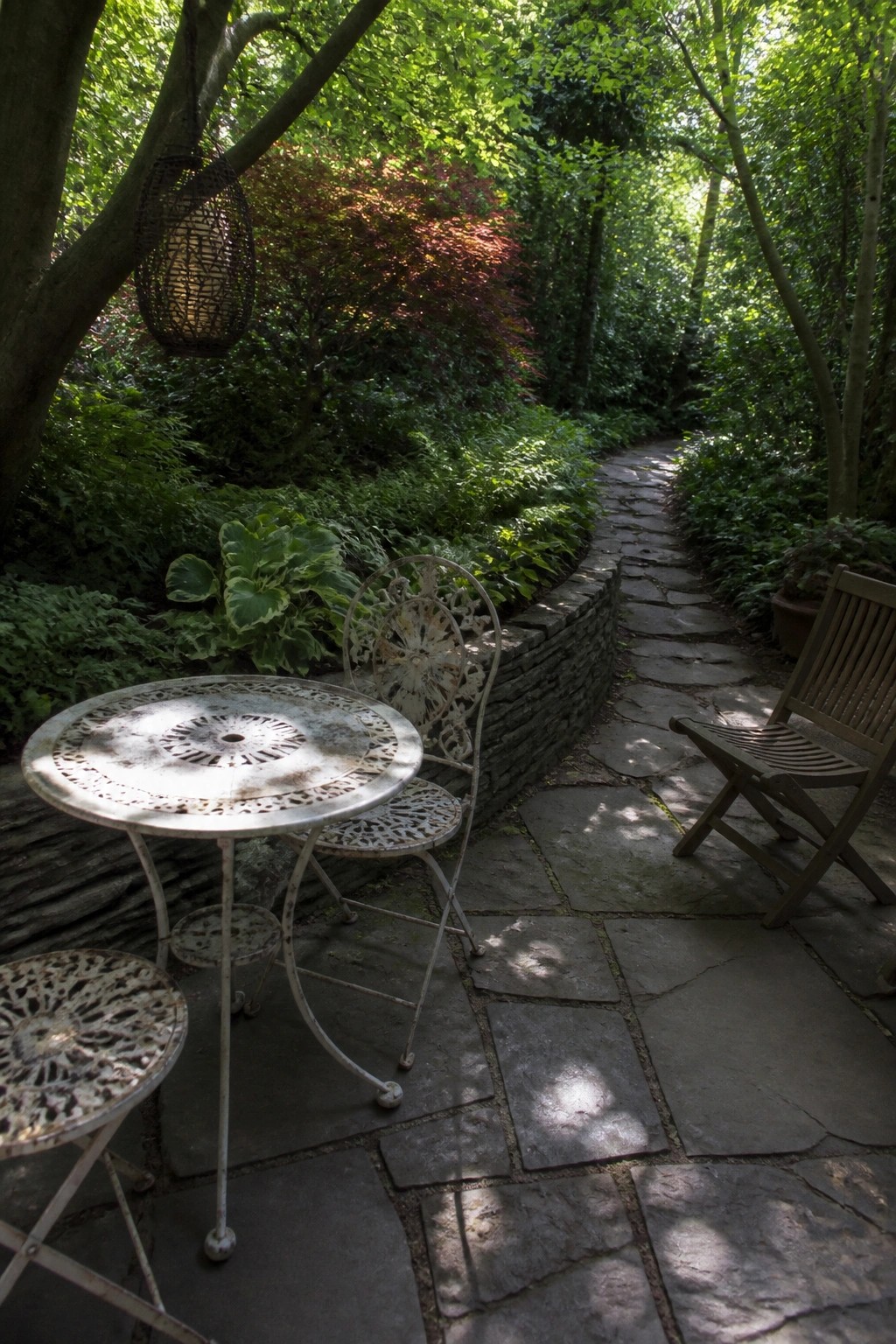 White ornate metal table and chairs on stone path in lush garden