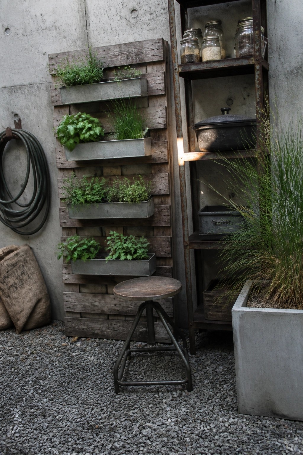 Pallet wood vertical herb garden beside rusty shelves and stool on gravel