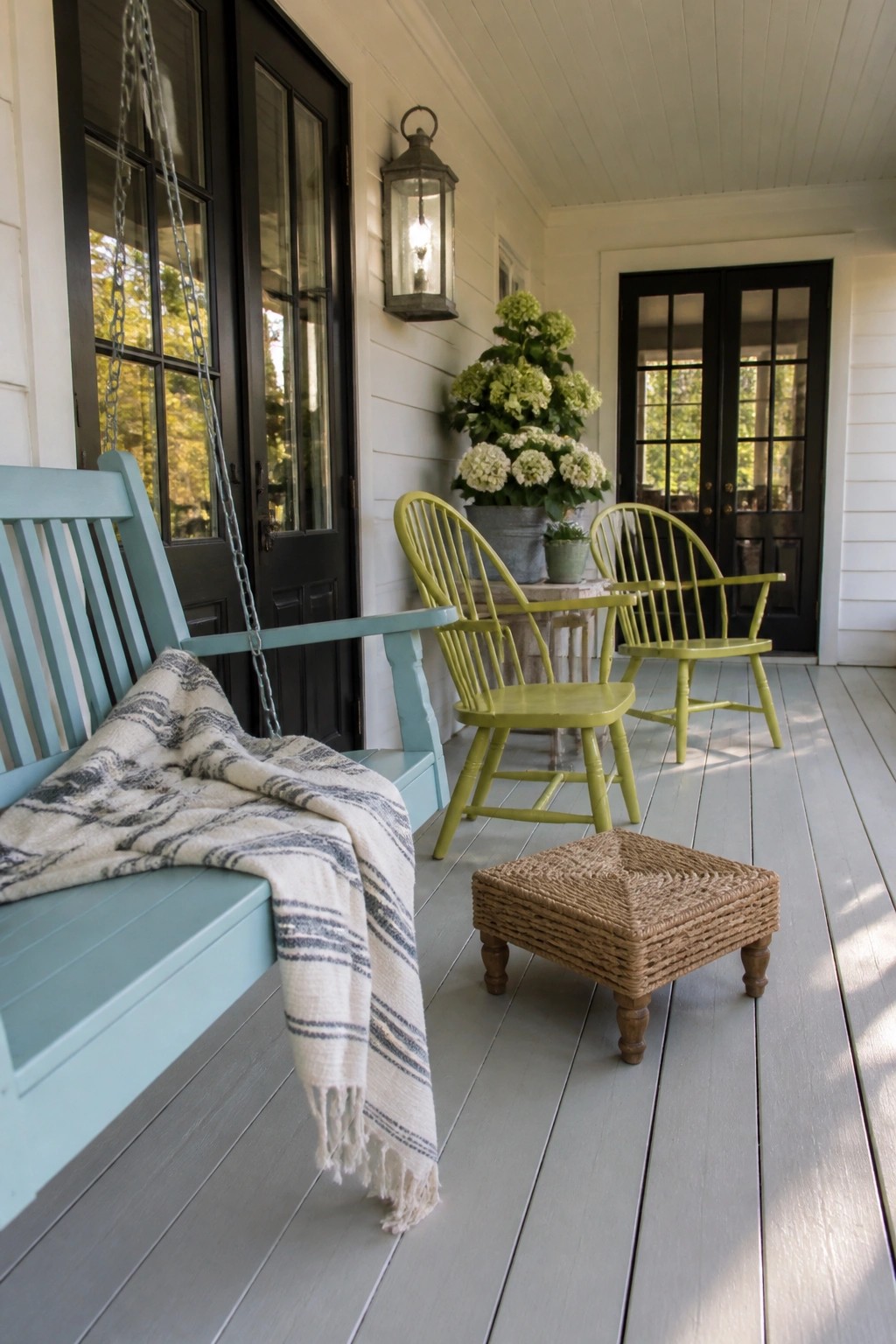 Light blue porch swing with blanket beside lime green chairs and woven stool on deck