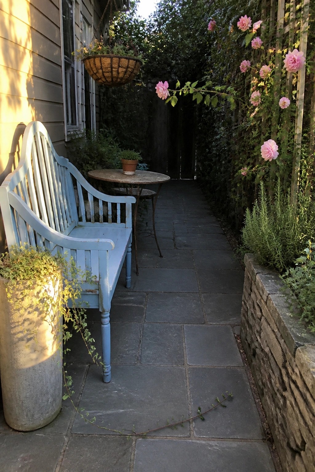Pale blue garden bench and table on slate path amid pink climbing roses