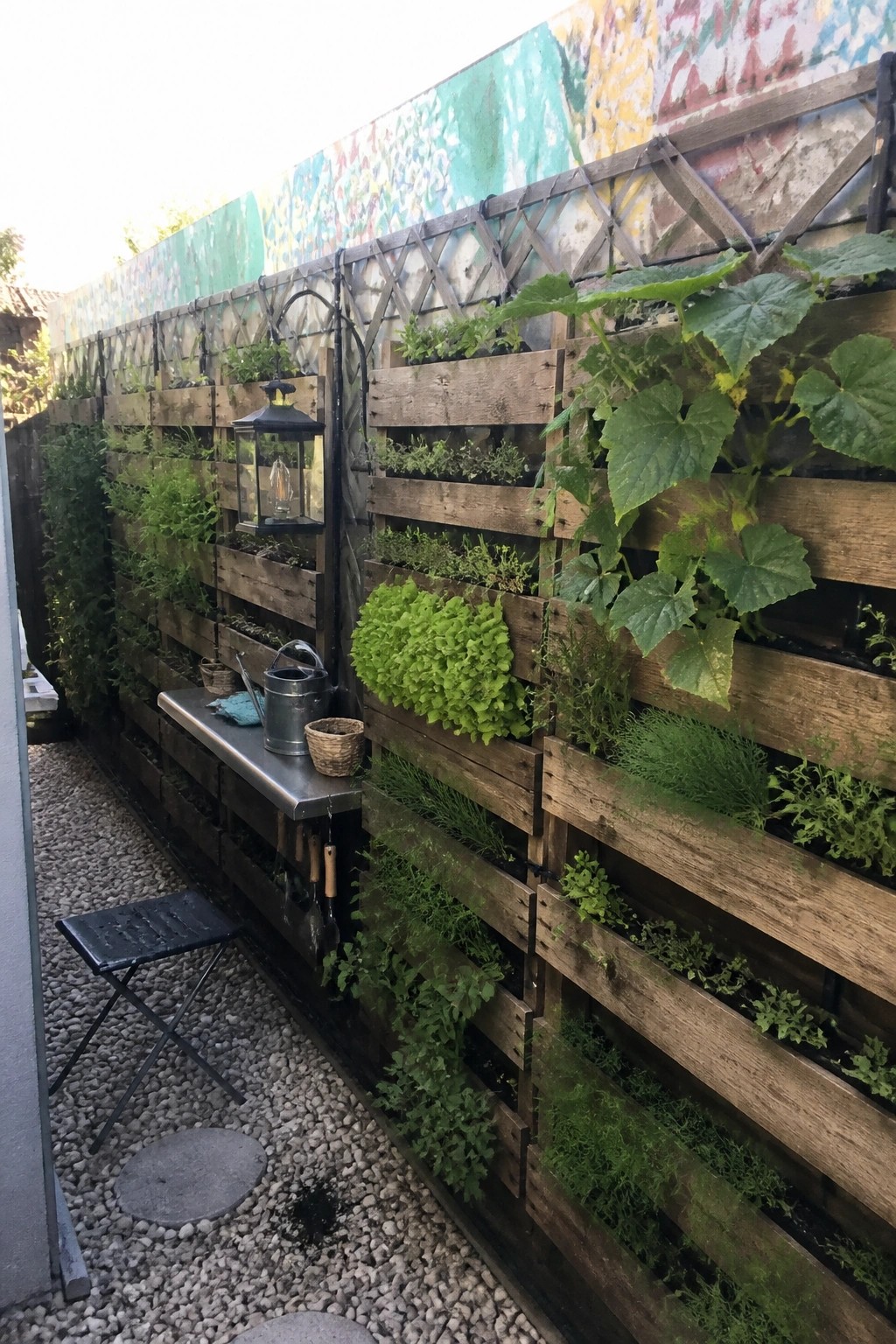 Vertical wooden planters bursting with green herbs against colorful graffiti wall on gravel patio