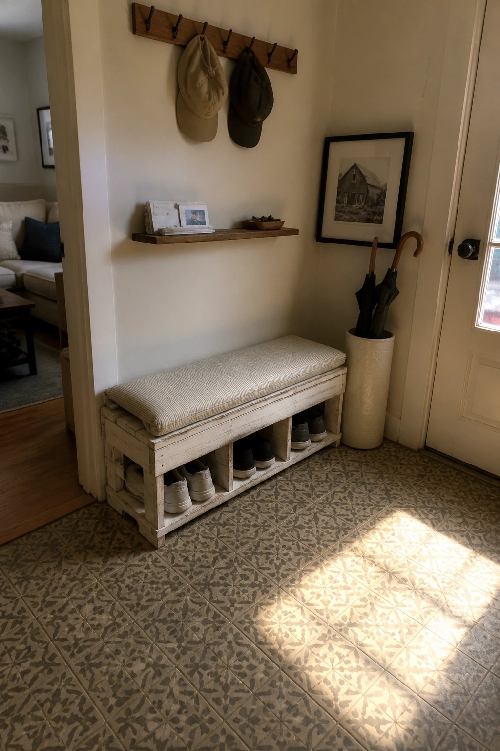 White wooden bench with cushion and shoe storage under hooks with caps and umbrella stand.