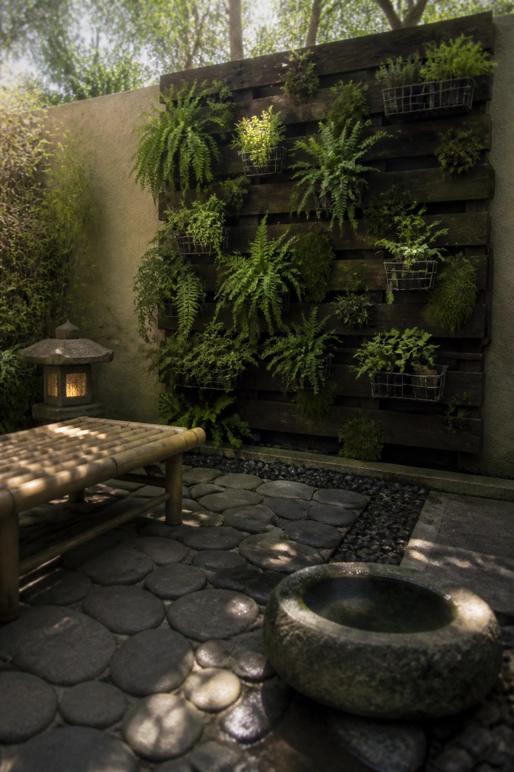 A wooden pallet mounted on an outdoor wall holds ferns and other plants in wire baskets, with a bamboo bench and stone path visible in the foreground.