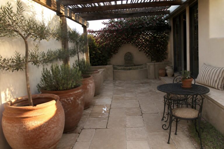 23 Lush Patio Garden Ideas Designed for Container Planting Courtyard with terracotta pots, stone fountain, bistro table and chairs under pergola