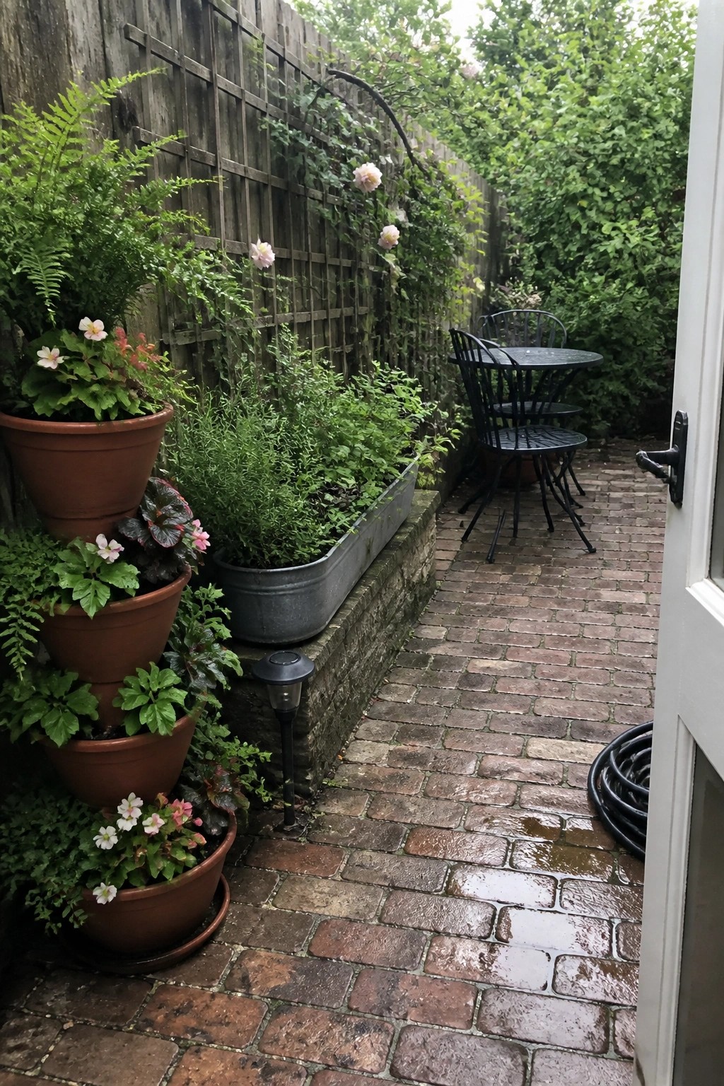 Wet brick patio with stacked flower pots, metal planter, and bistro set