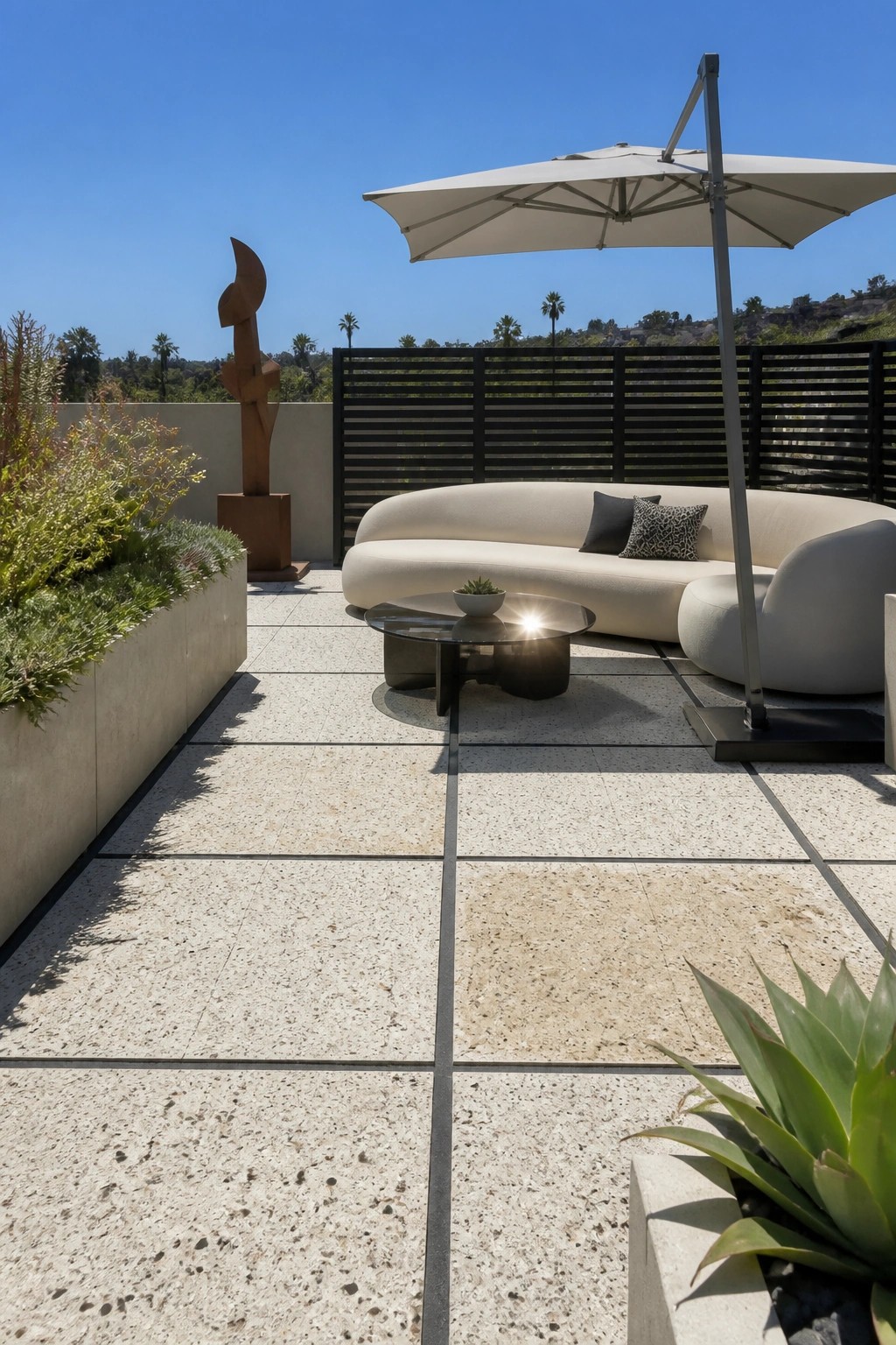 Modern patio with curved sofa, umbrella, glass table, sculpture on sunny stone terrace