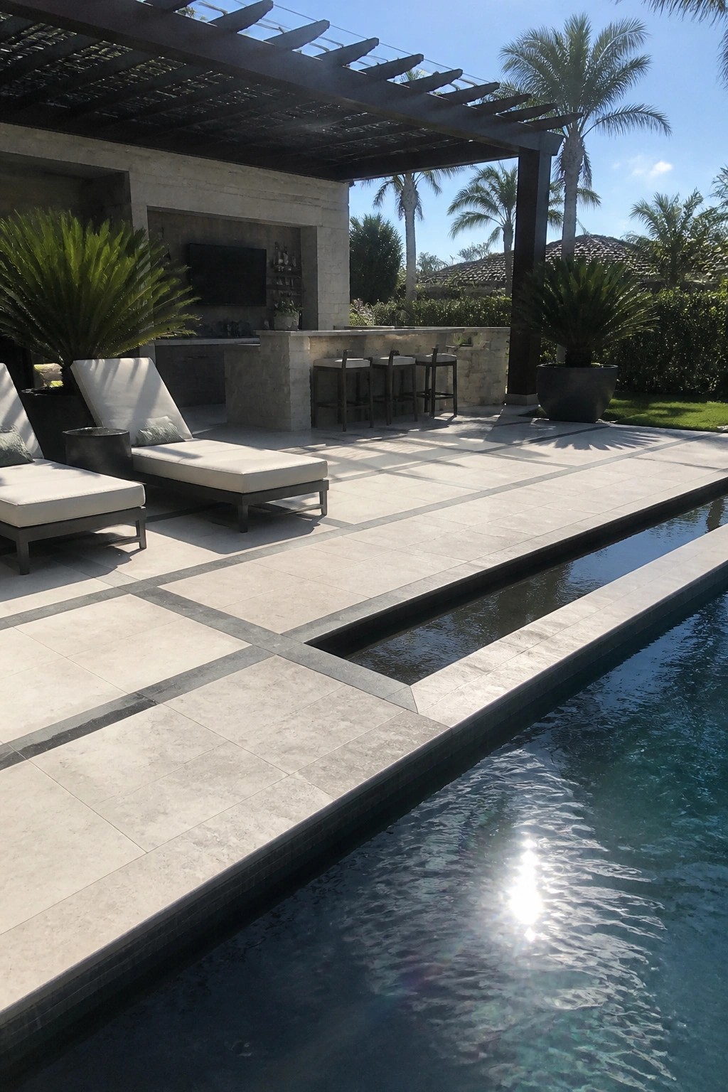Luxurious modern patio with lounge chairs, stone bar, swimming pool, and palm trees.
