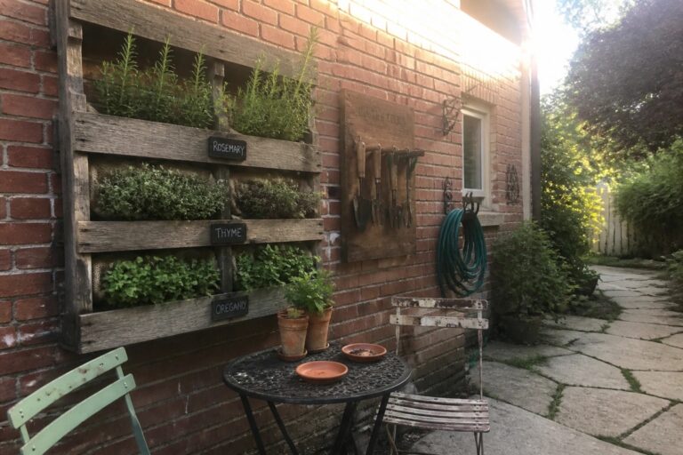 20 Clever Wall-Mounted Pallet Planter Ideas for Blank Outdoor Walls Rustic wooden herb planter on brick wall beside garden tools and patio table.