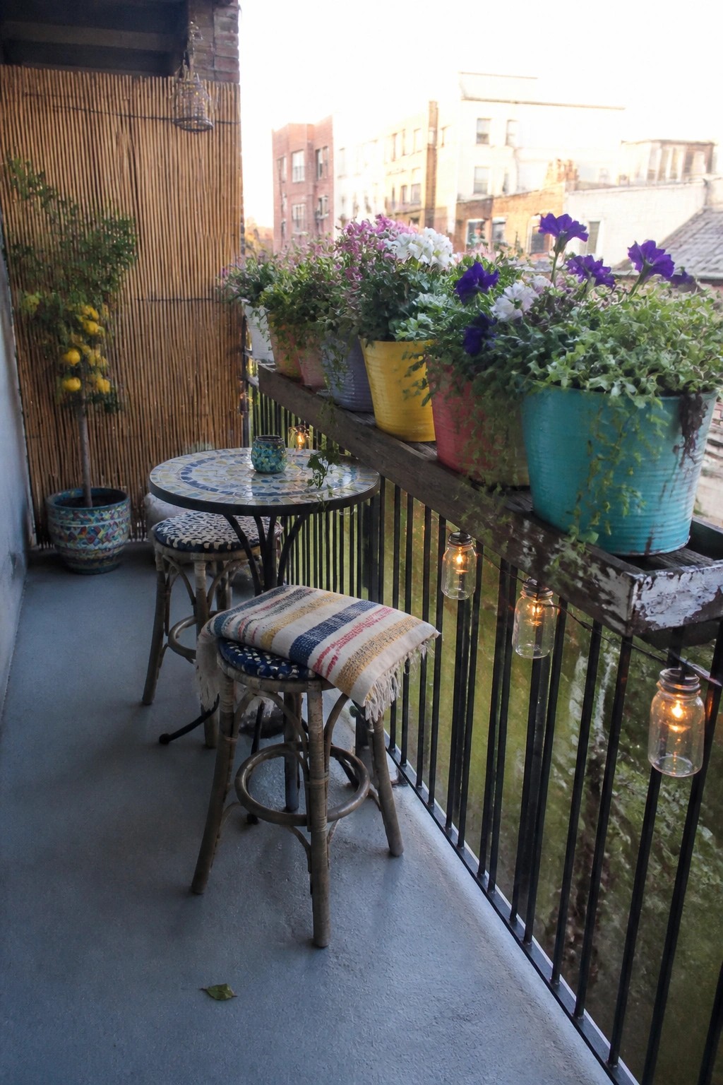 Cozy balcony with colorful potted flowers, mosaic table, stools, and string lights.