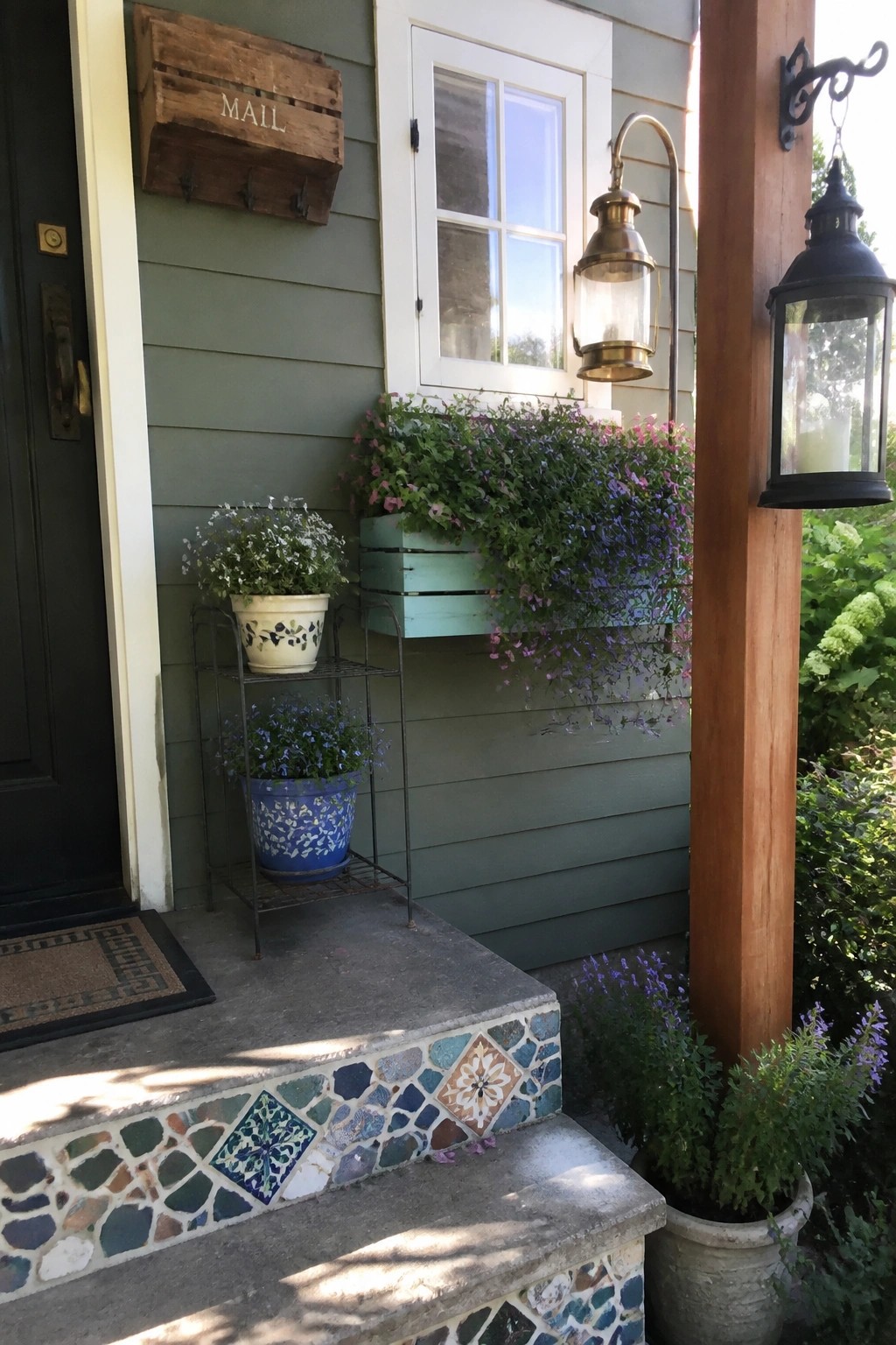 A green house exterior with two wooden pallet crates used as planters holding trailing pink and purple flowers, positioned near a window and door.