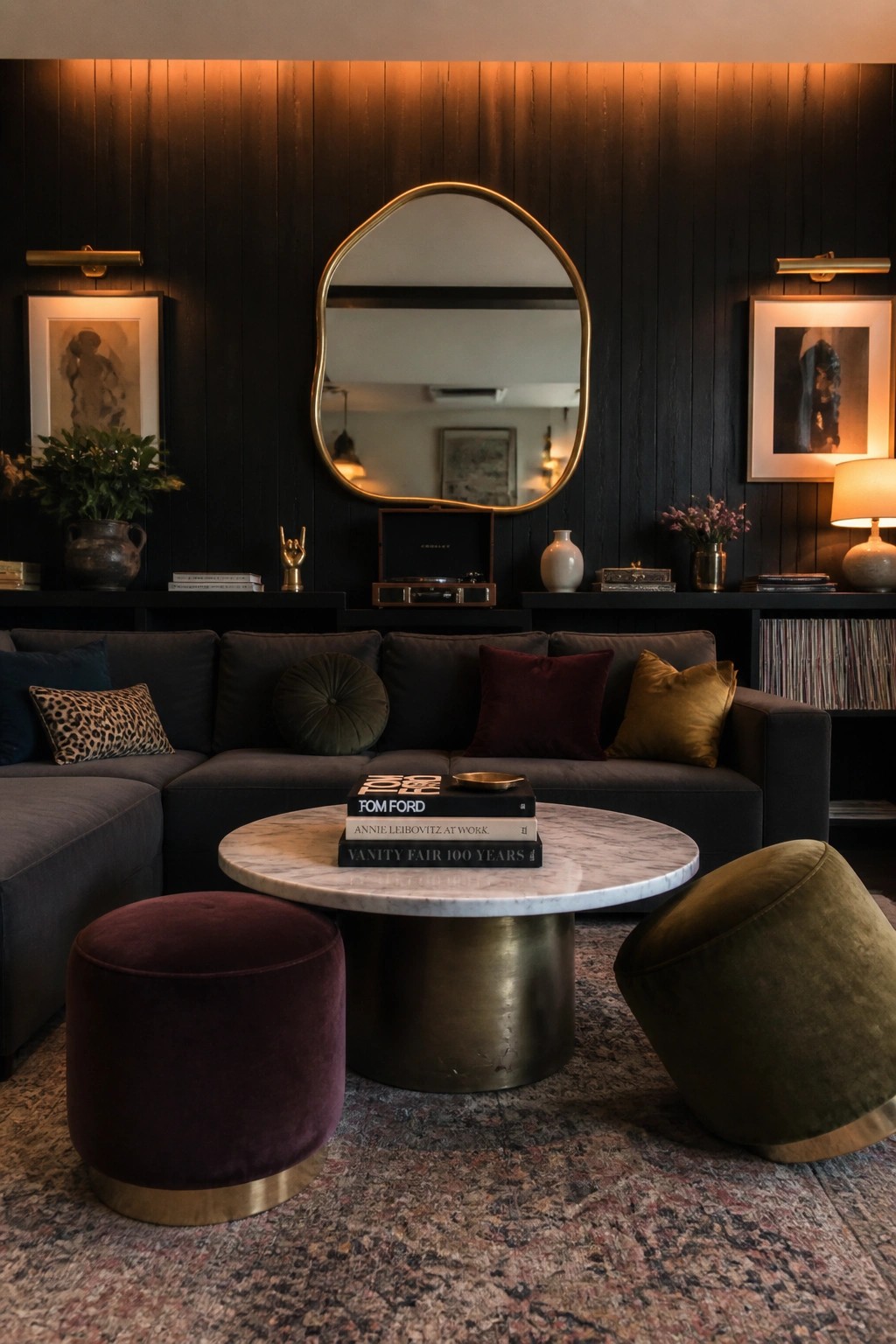 A living room featuring a dark vertical wood paneled accent wall with a large irregular gold mirror centered above a low shelf holding a record player and decorative items, in front of a gray sectional sofa with a round marble coffee table.