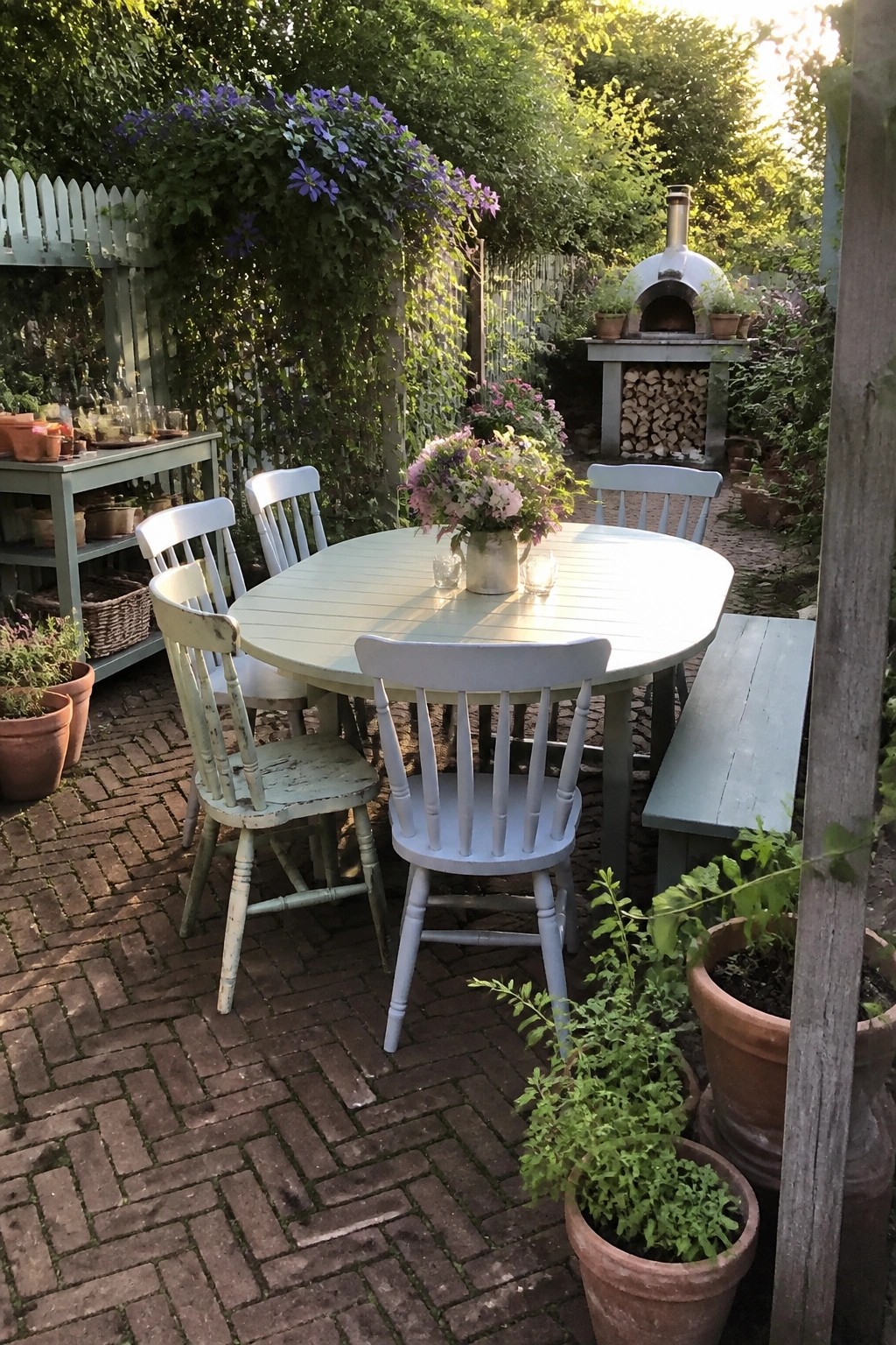 Round light blue table with white chairs and flowers on brick garden patio