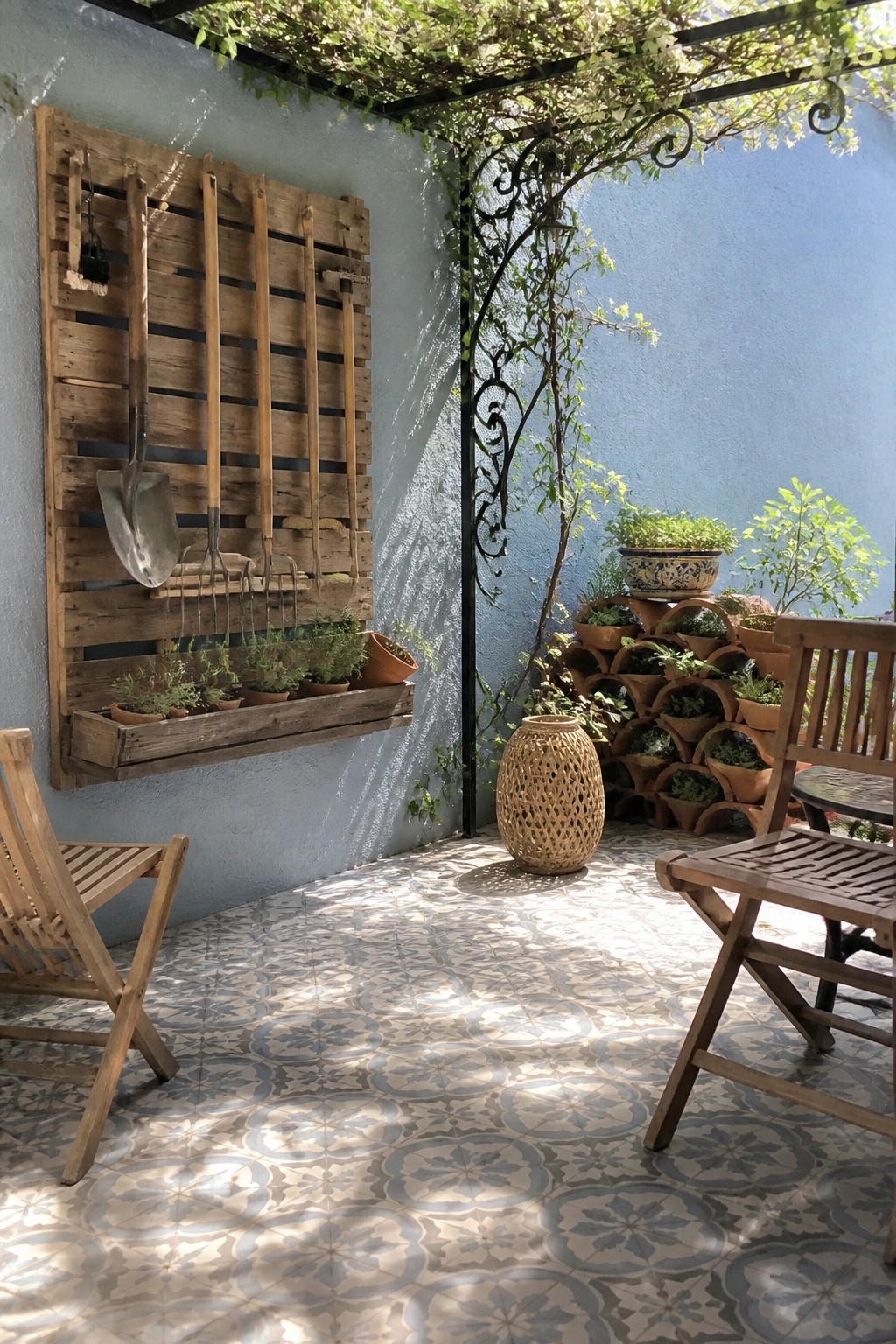 Shaded patio with wooden tool rack, stacked pots, chairs on patterned tiles