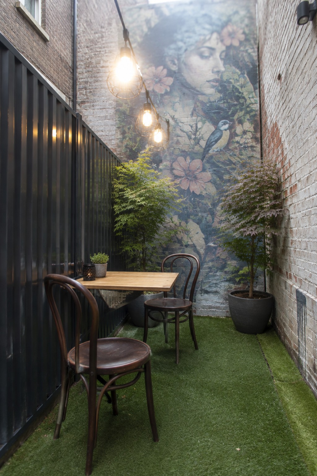 Outdoor patio with wooden table, chairs, string lights, plants, and floral mural