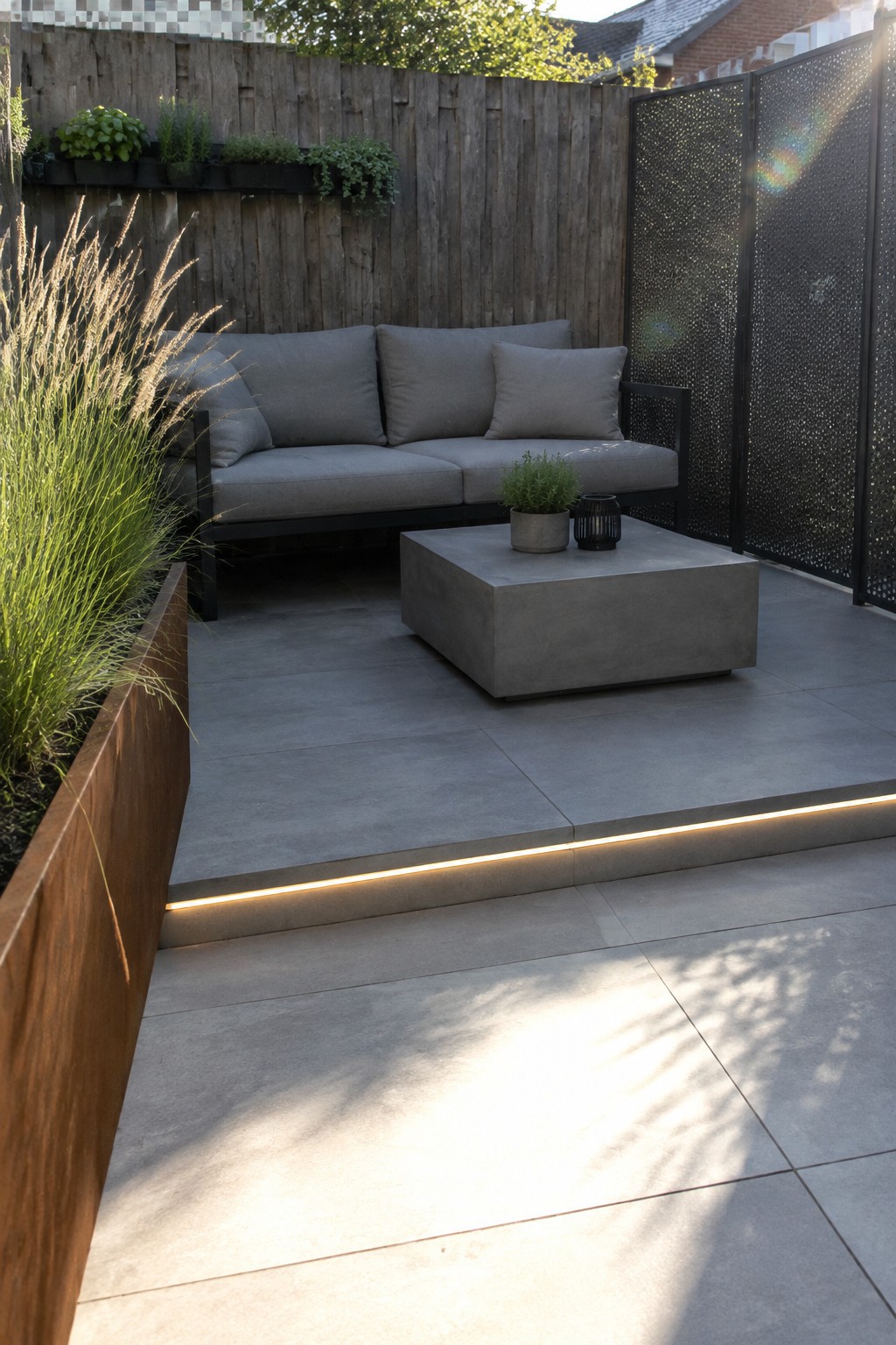 Modern gray sofa and concrete table on sunlit patio with grasses and LED lighting