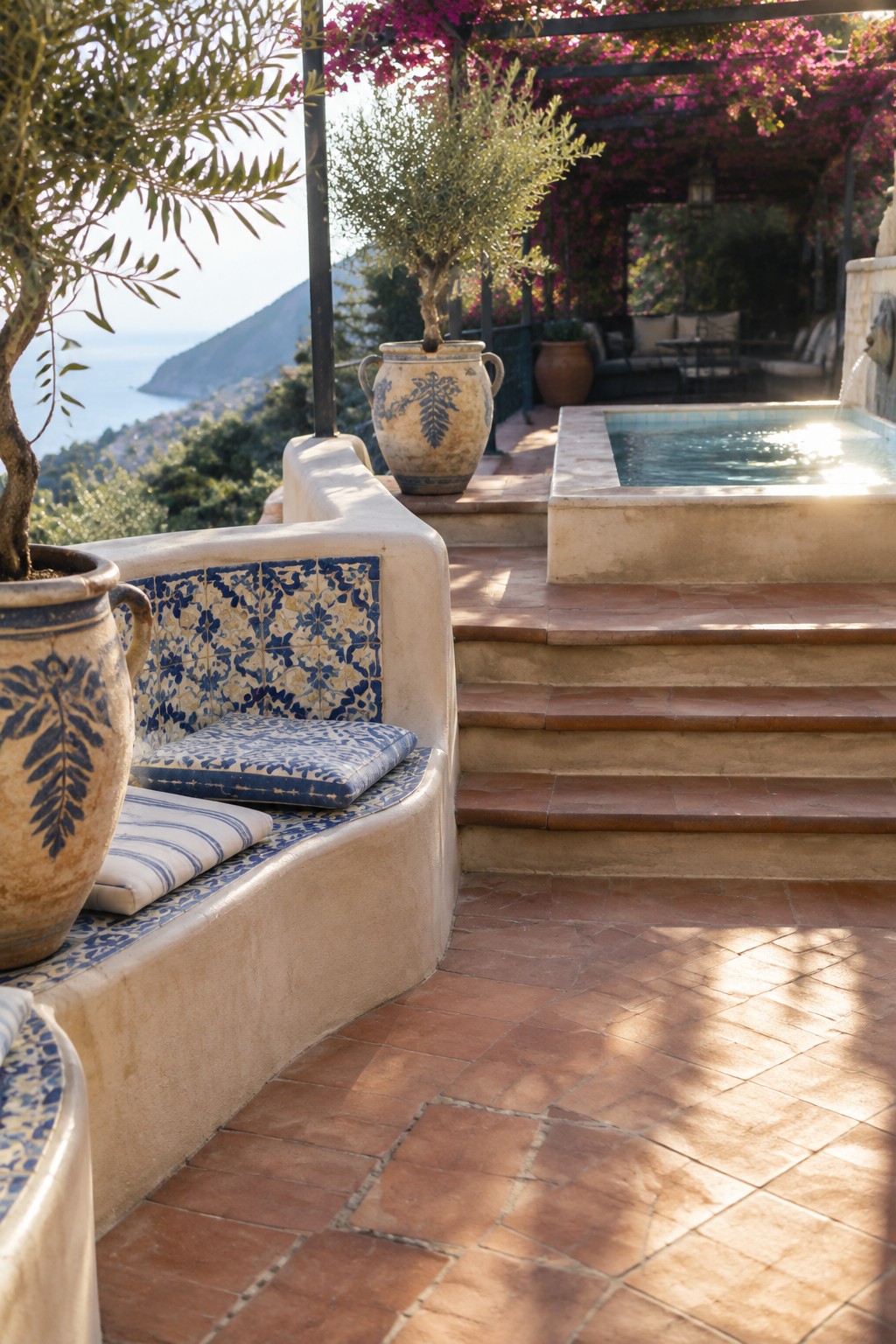 A terraced patio with curved built-in seating covered in blue and white patterned tiles, steps leading to a small pool, and potted plants on a hillside.