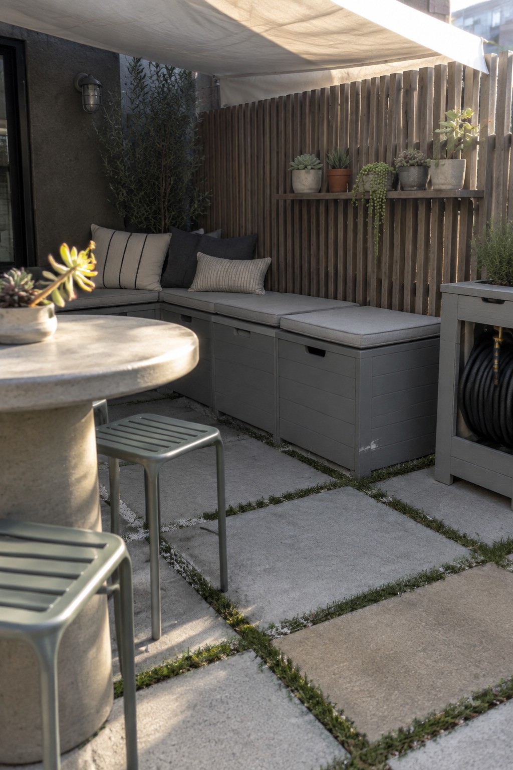 Modern patio with gray storage benches, cushions, succulents on wooden fence, concrete table and stools