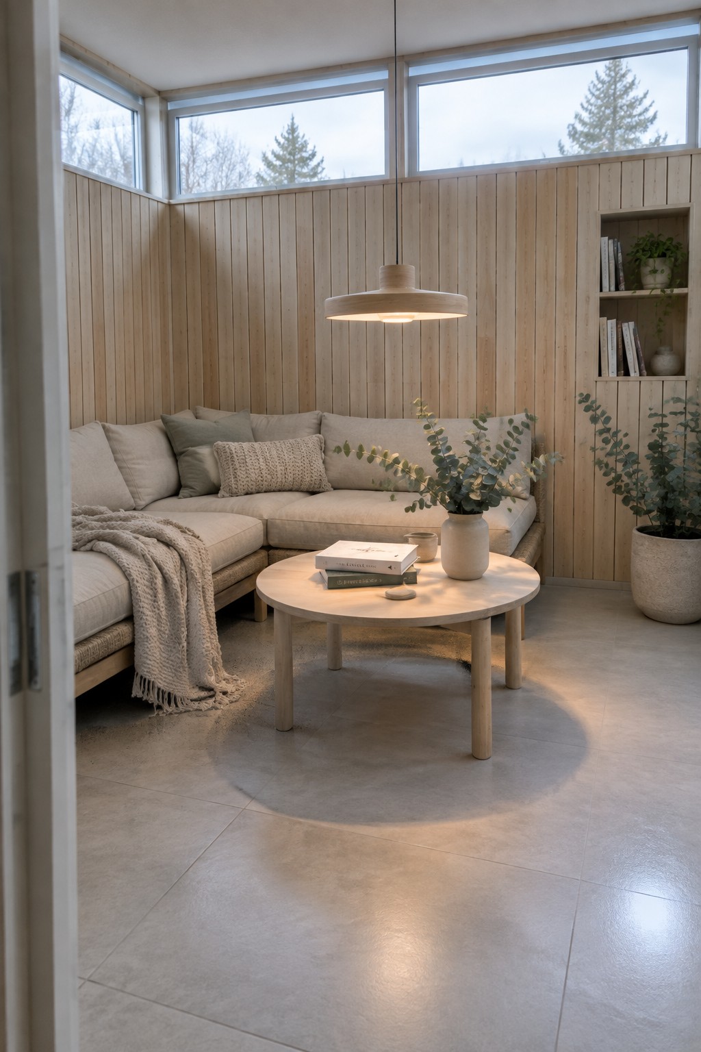 Cozy light wood nook with beige sectional sofa, round table, books, and pendant light