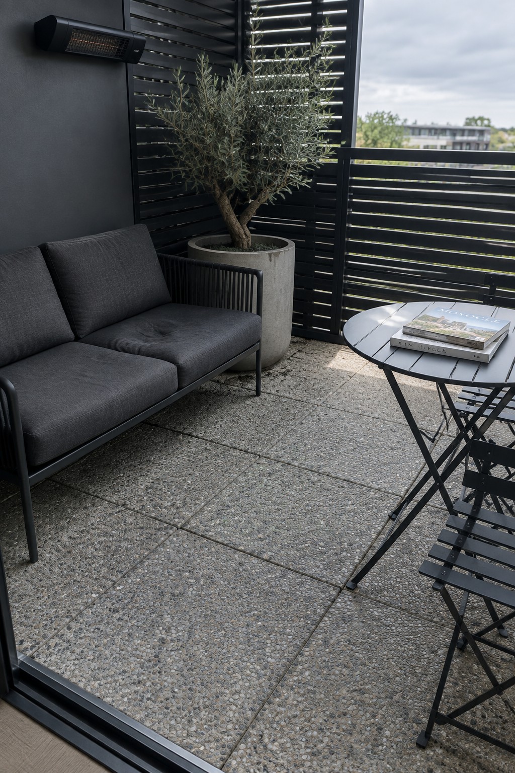 Modern balcony with dark gray sofa, potted olive tree, and round black table
