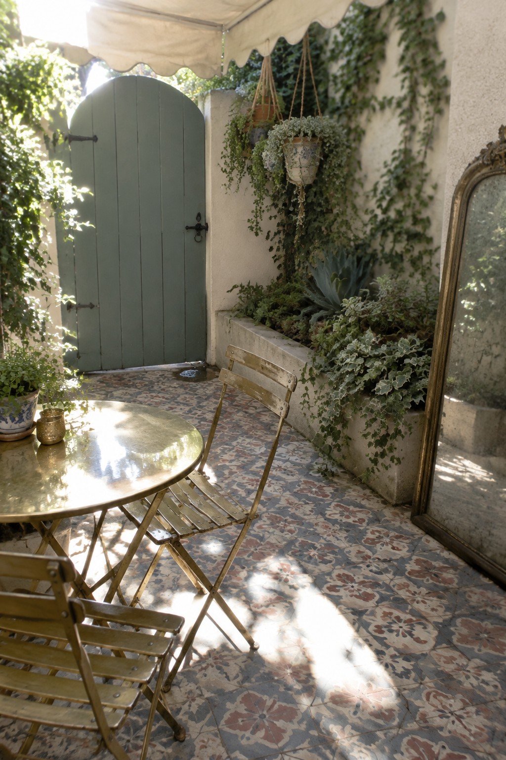 Sunny patio with brass table, chairs on floral tiles, green door, plants and mirror