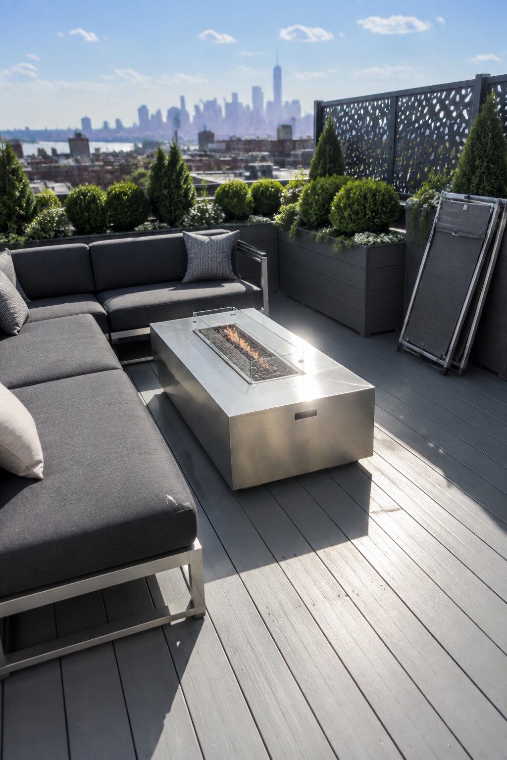 Modern rooftop deck with gray sectional sofa, fire pit, and NYC skyline view