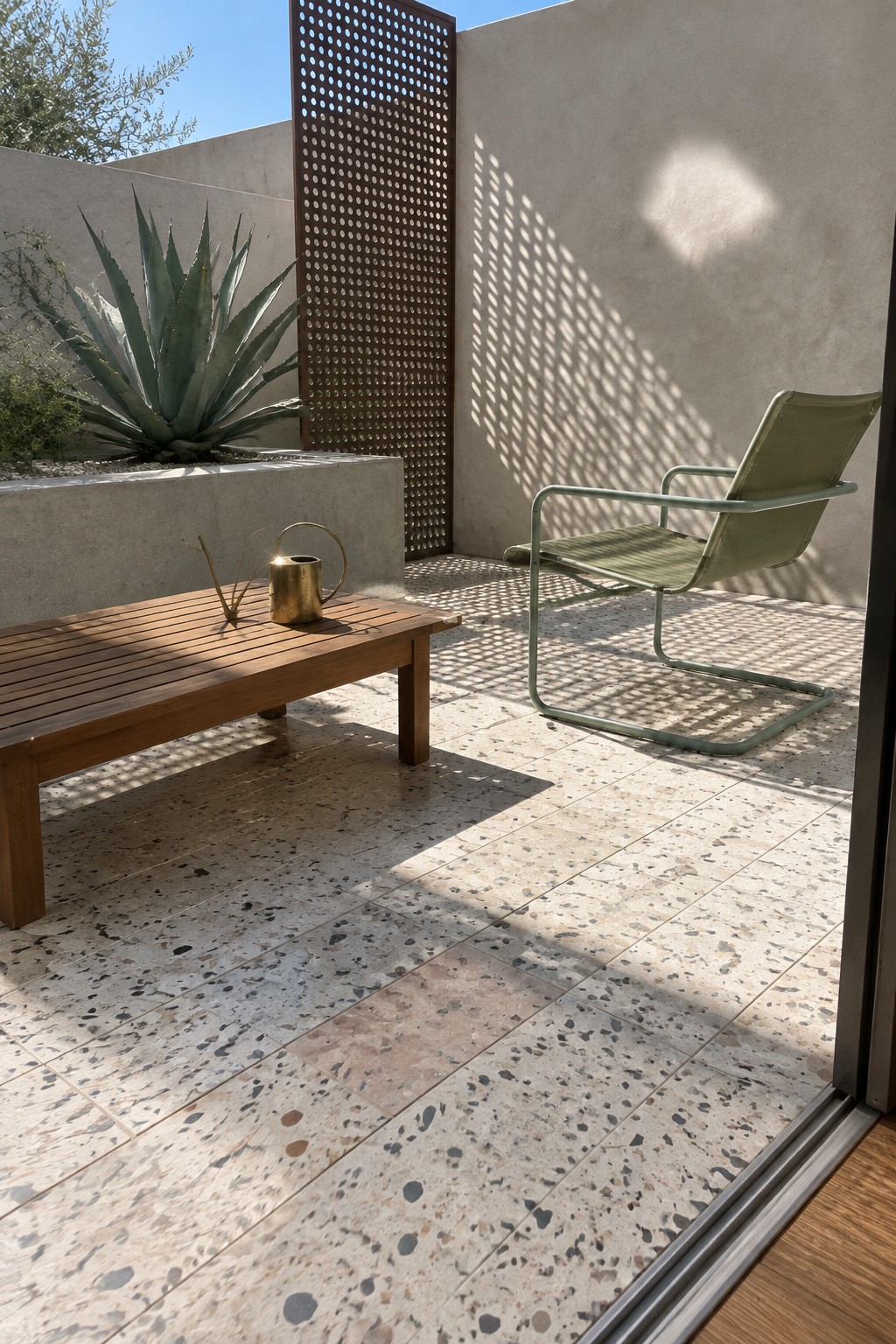 Modern patio with wooden bench, green chair, agave plant, and speckled terrazzo floor in sunlight