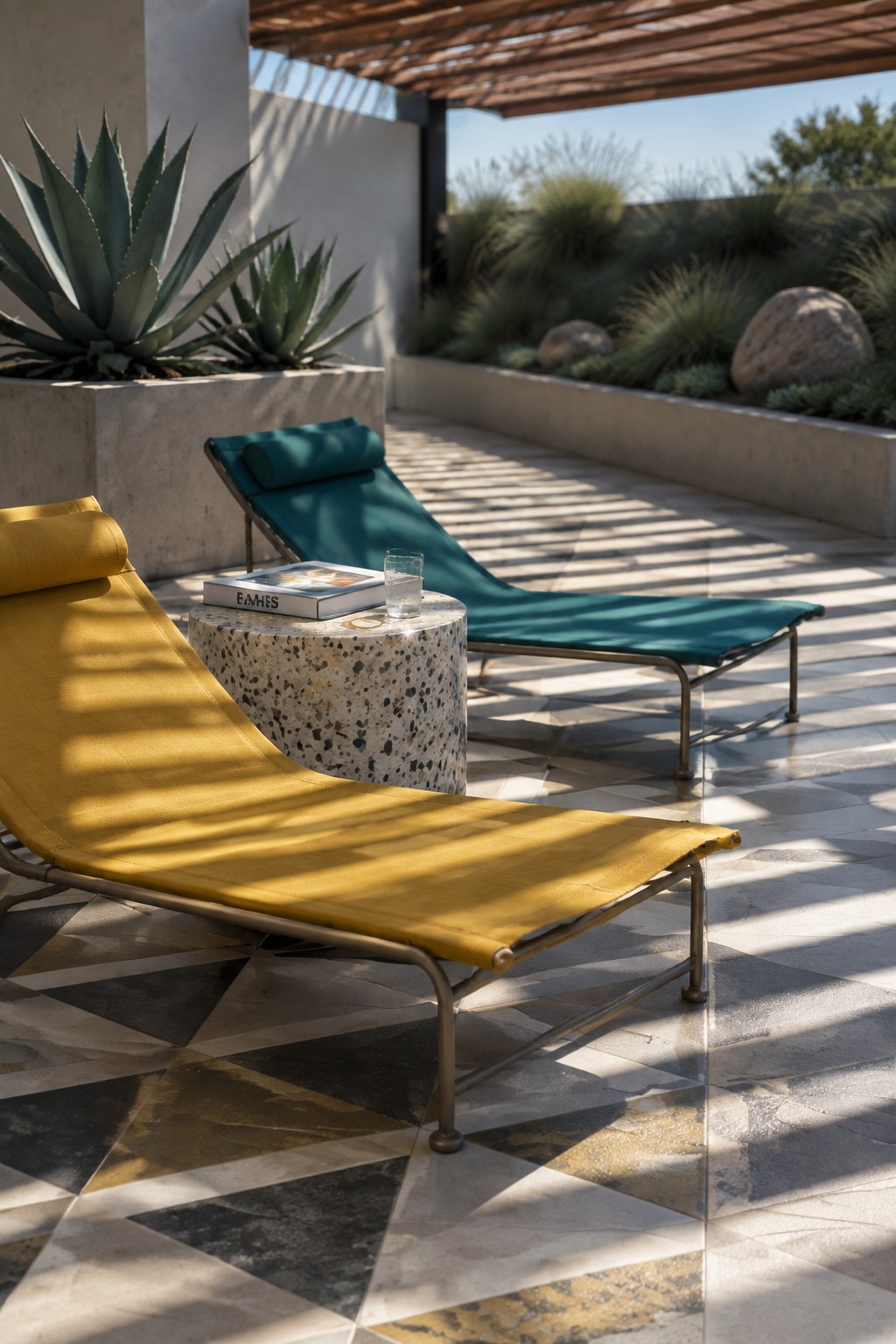 Yellow and teal lounge chairs with terrazzo table on sunlit geometric tiled patio