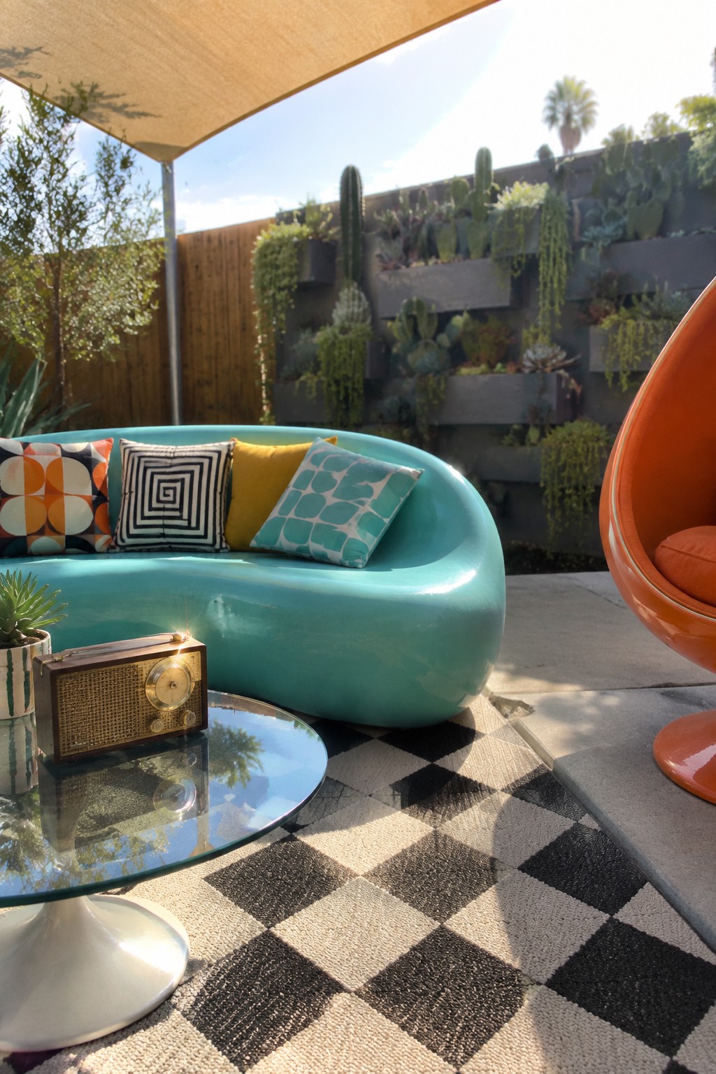 Vibrant patio with turquoise sofa, orange egg chair, checkered rug and succulent wall