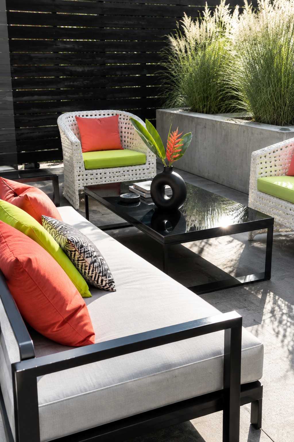 White wicker sofa with red-green pillows beside black coffee table and floral vase.