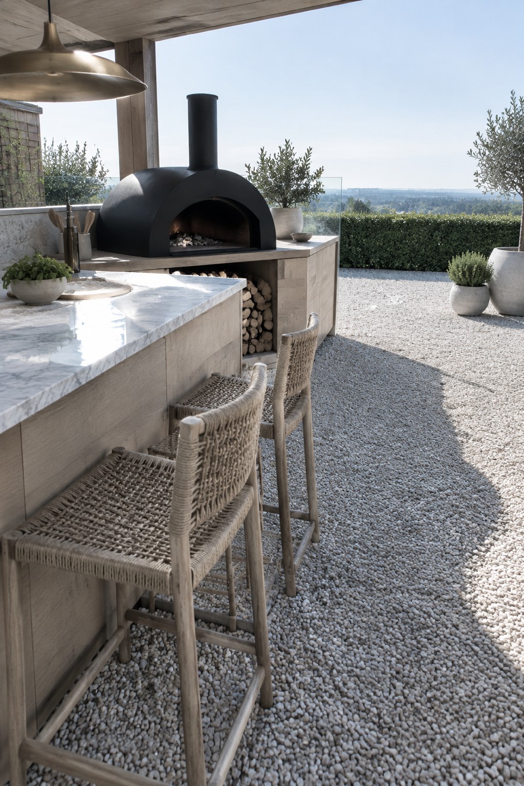 A black built-in outdoor pizza oven set into a light wood counter with woven bar stools on a gravel patio.