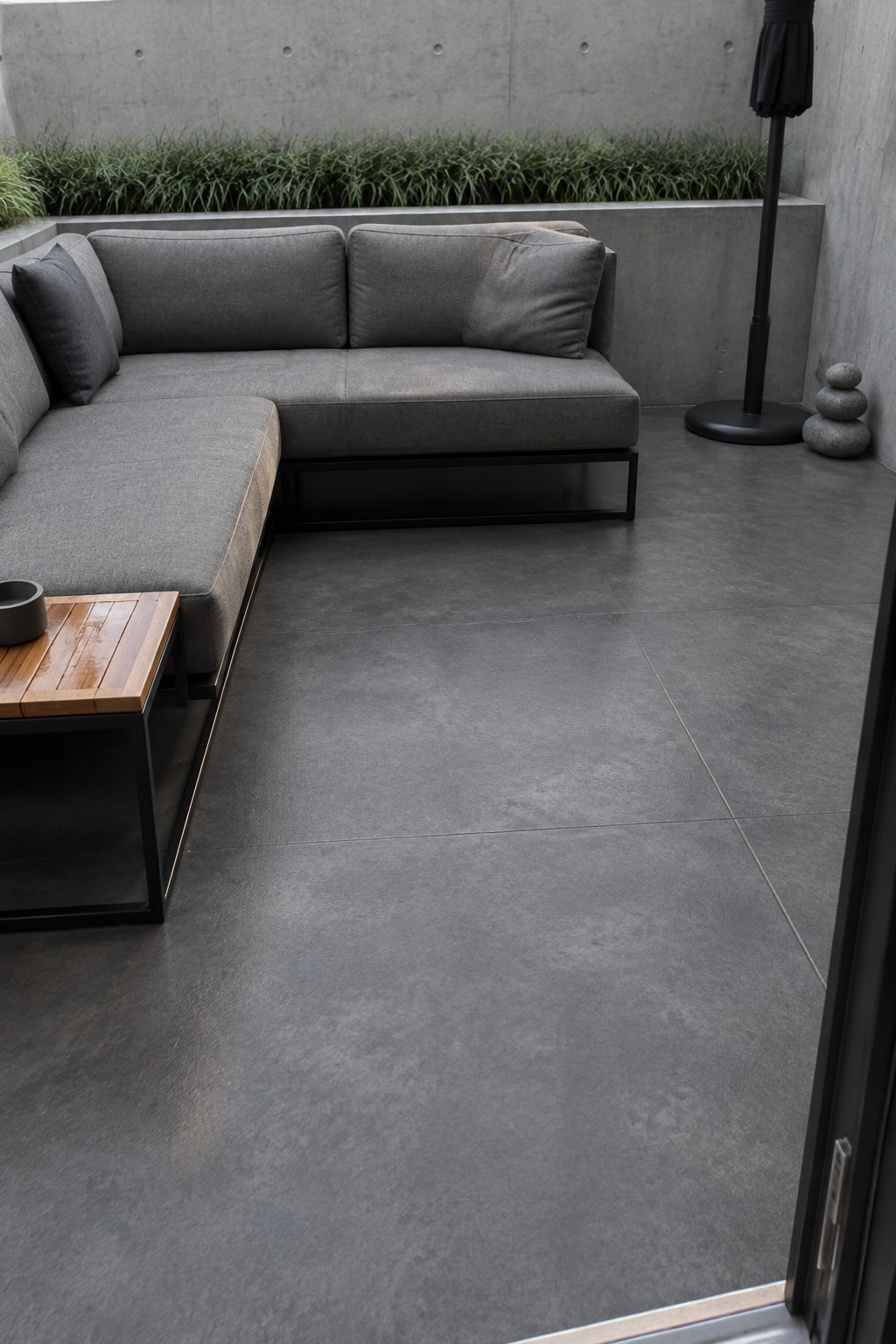 Modern gray L-shaped sectional sofa on dark tiled concrete patio with wooden table