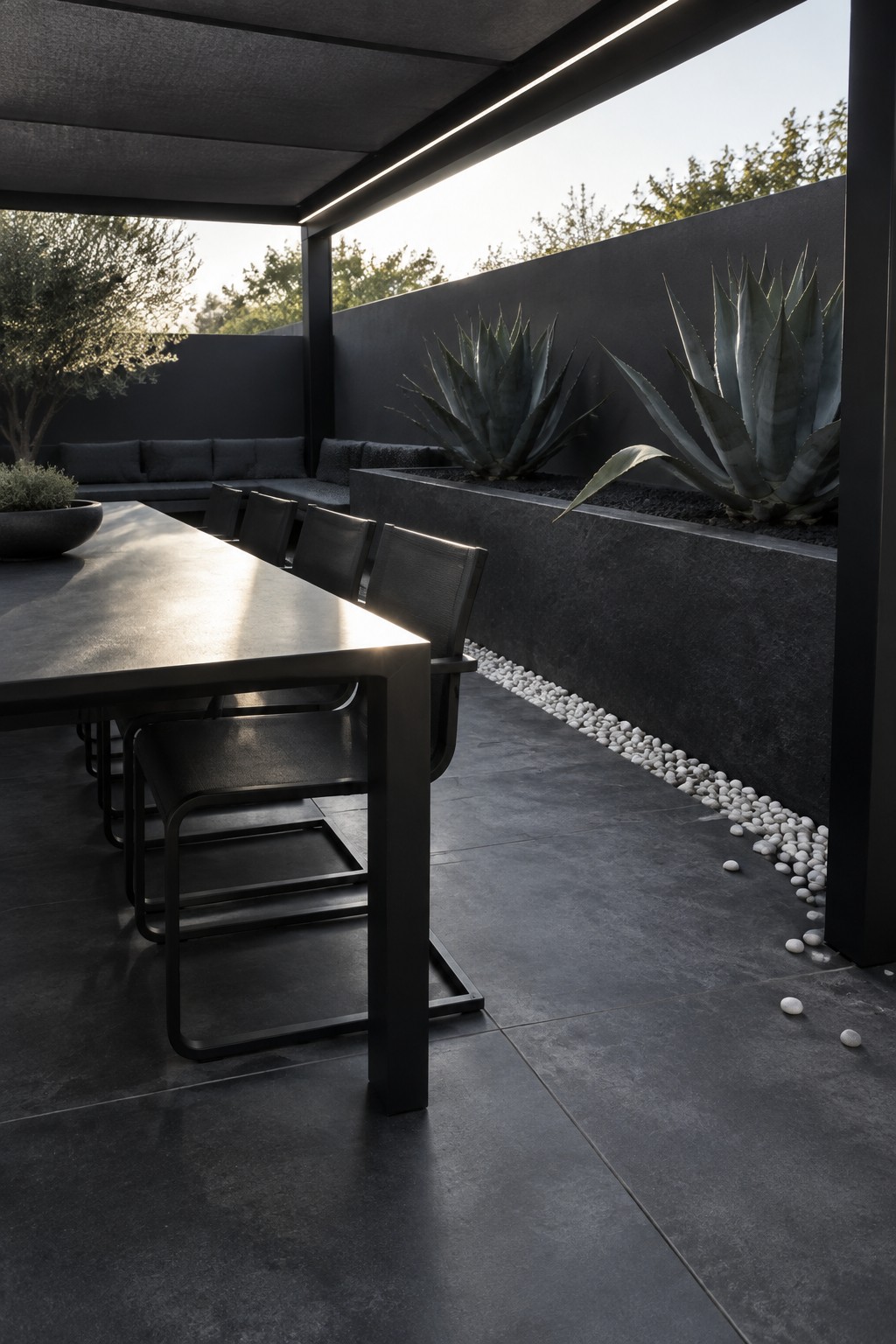 Dark modern patio with black dining table, chairs, agave plants, and white pebbles