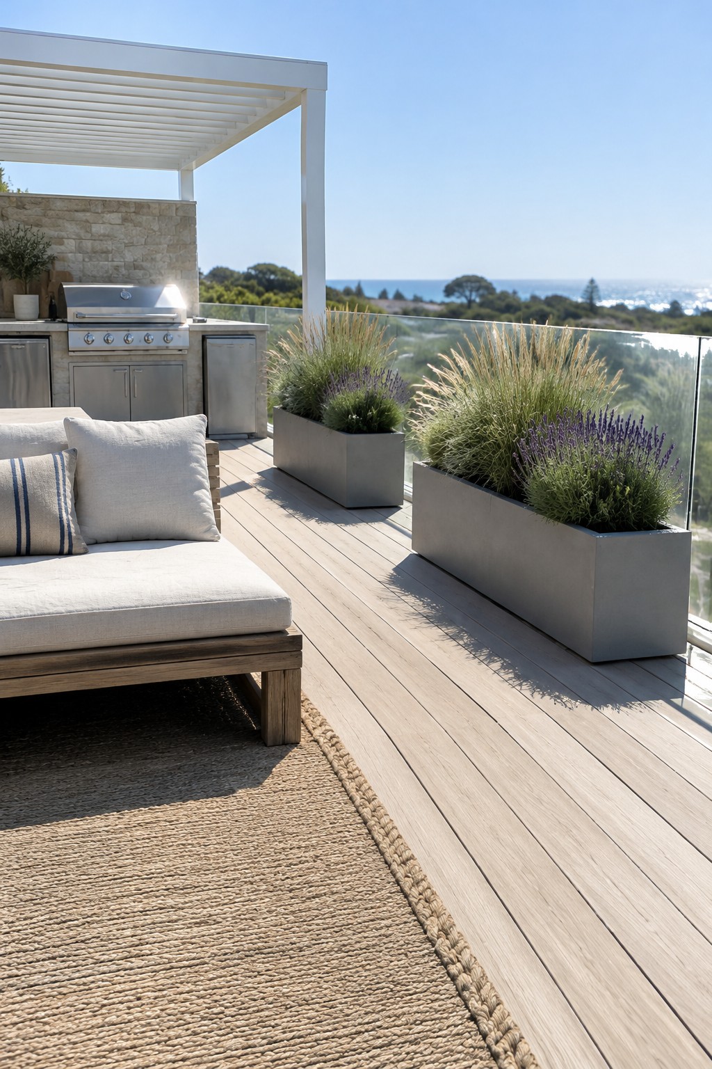 Long rectangular planters filled with grasses and purple flowers line the glass railing of a wooden patio.