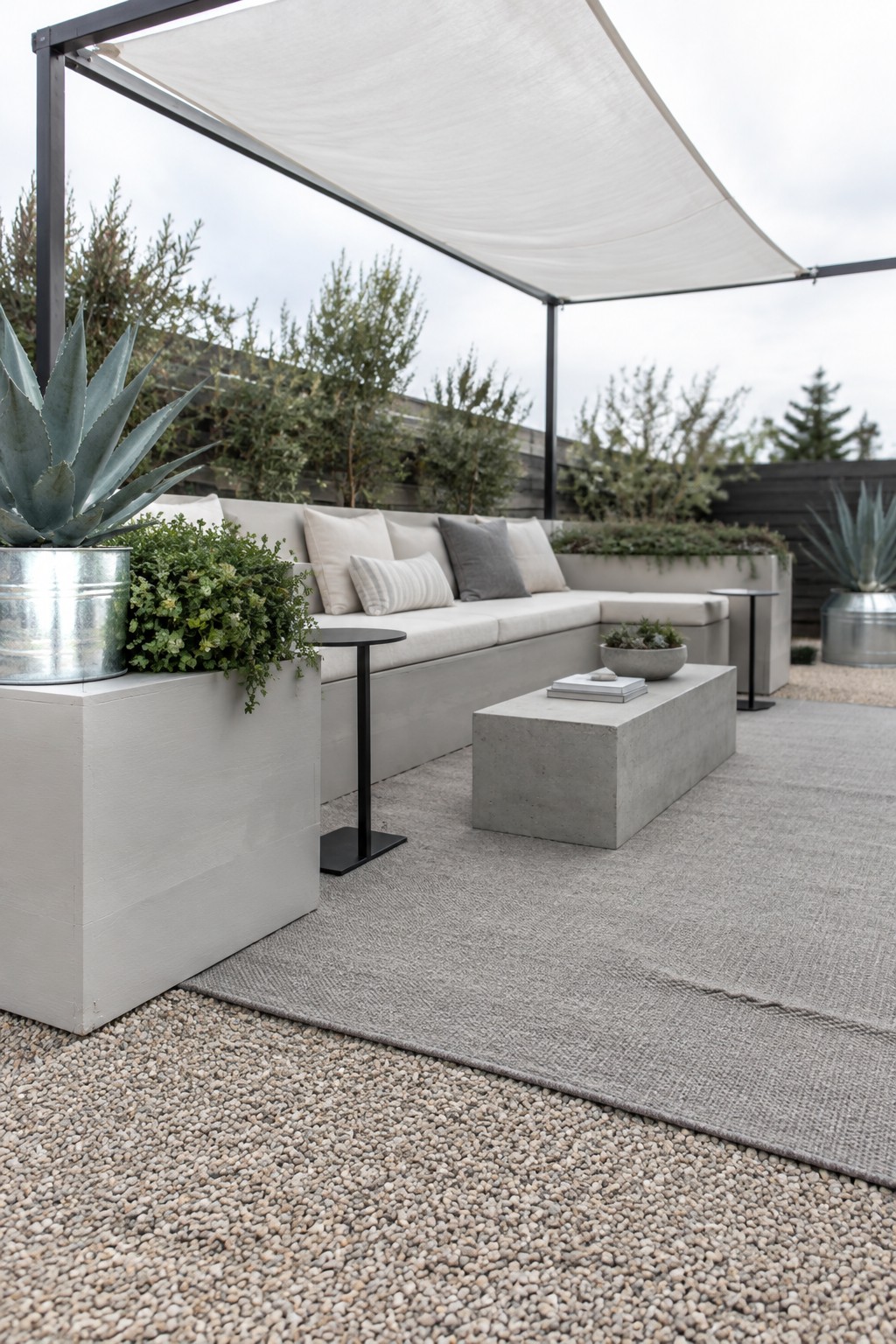 A white fabric canopy on a dark metal frame shades a built-in patio sofa and concrete coffee table.