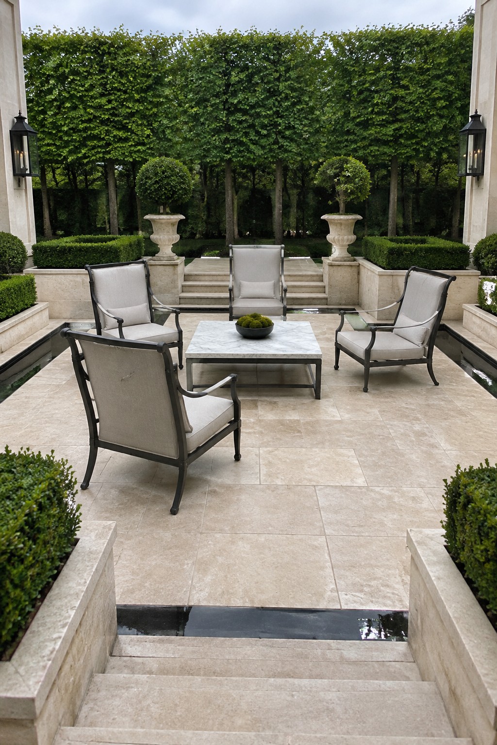 Four cushioned chairs surround a low rectangular table on a pale stone patio with large square pavers.