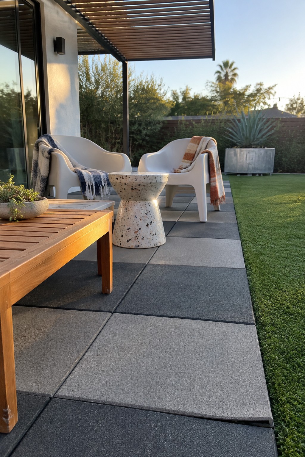 Large gray concrete slabs form a patio beside white outdoor chairs and a wooden table.