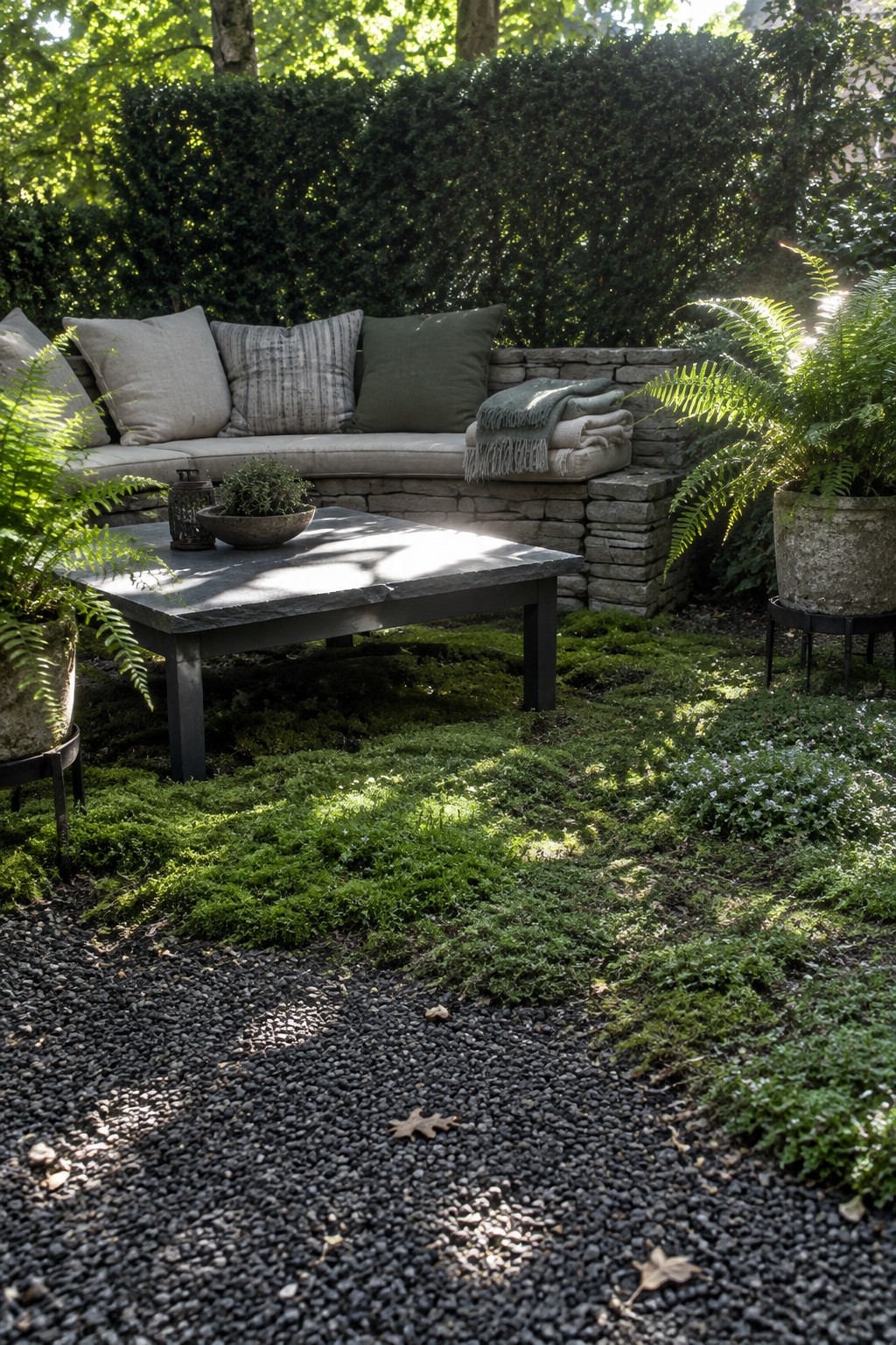 A stone bench and low table sit above mossy ground, with a gravel path in the foreground.