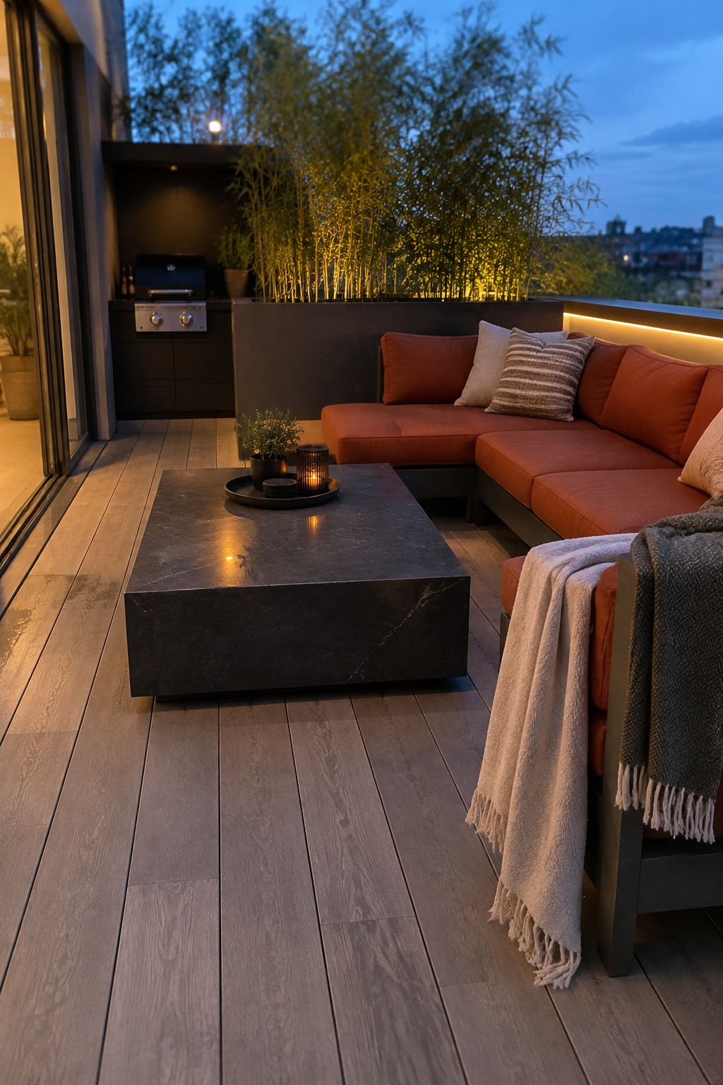 Long wood-look deck boards run along a terrace beside an orange sectional sofa and a built-in grill.