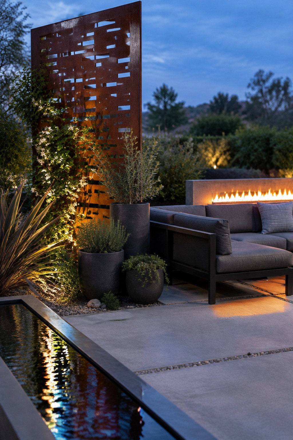 A tall rust-colored metal screen stands beside outdoor sofa seating, planters, and a narrow reflecting pool.