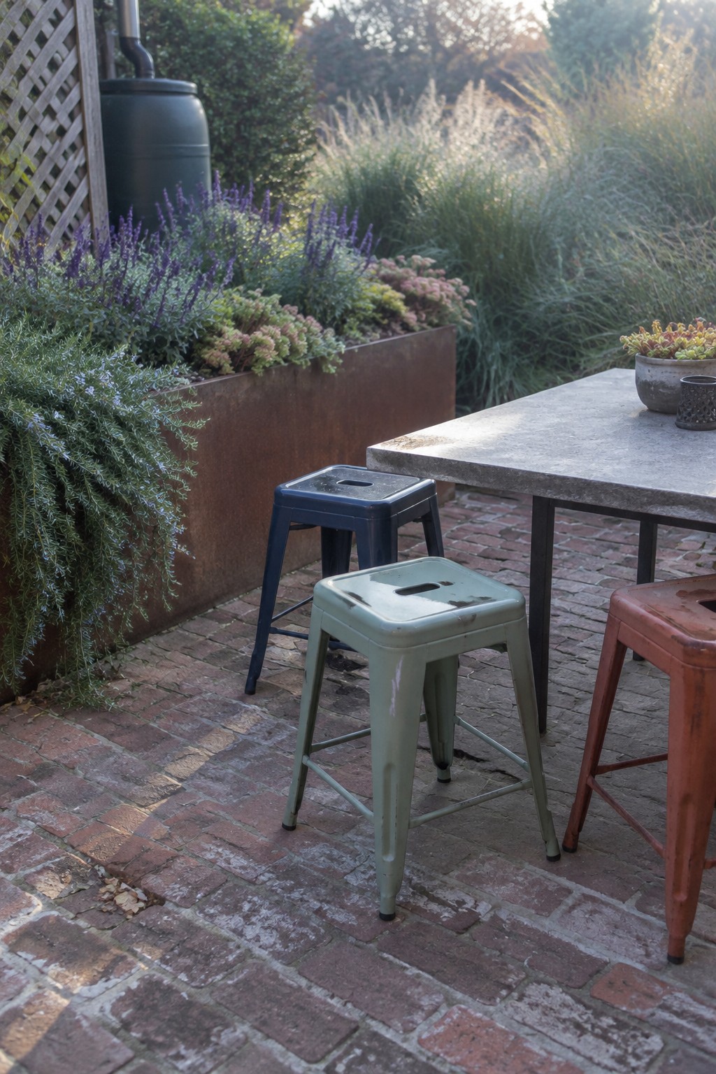Three metal stools sit around a rectangular outdoor table on a brick patio beside raised planters.
